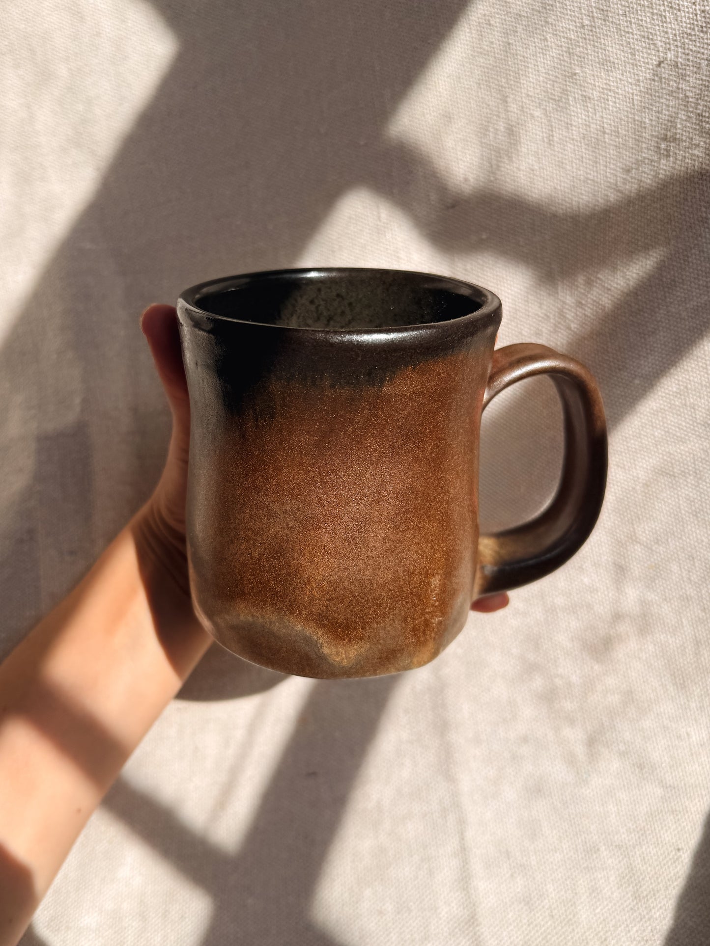 Hand holding a brown ceramic mug against a neutral background