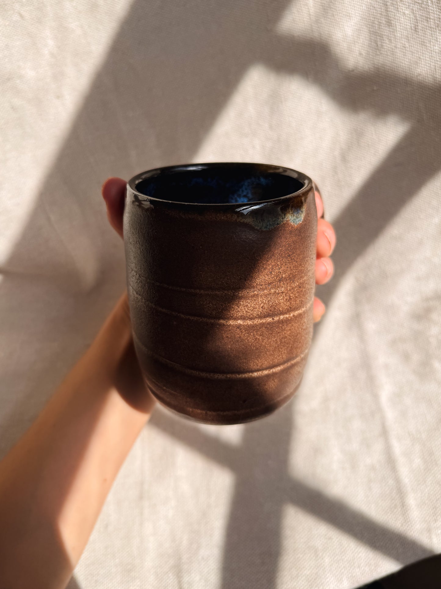Hand holding a brown ceramic mug against a textured light background