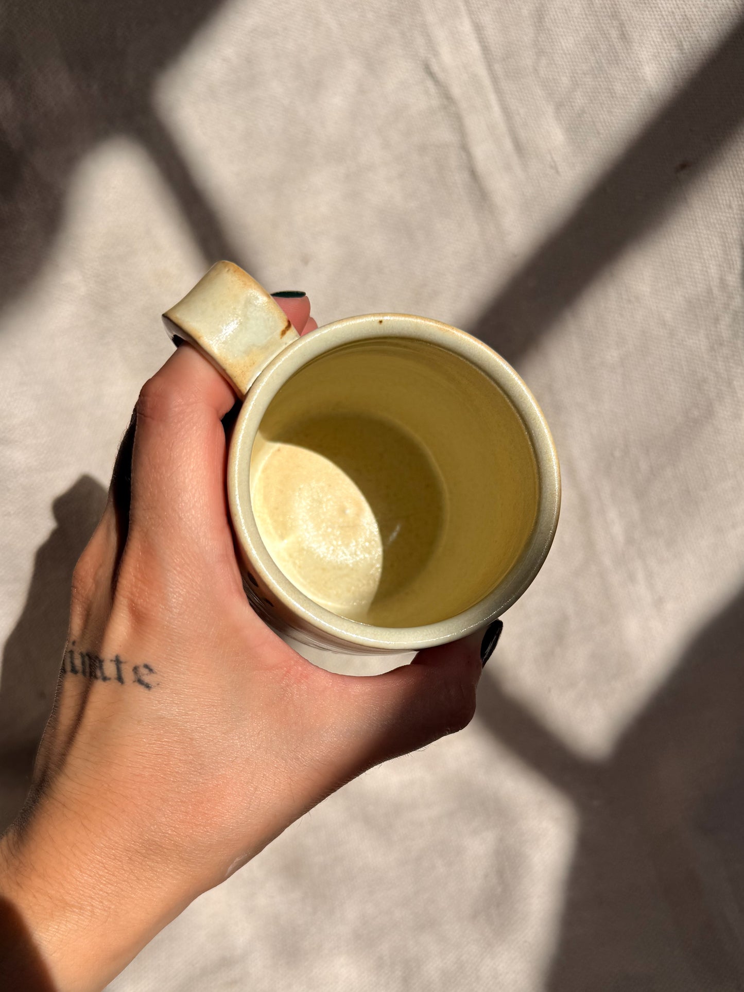 Hand holding a yellow ceramic cup against a neutral background