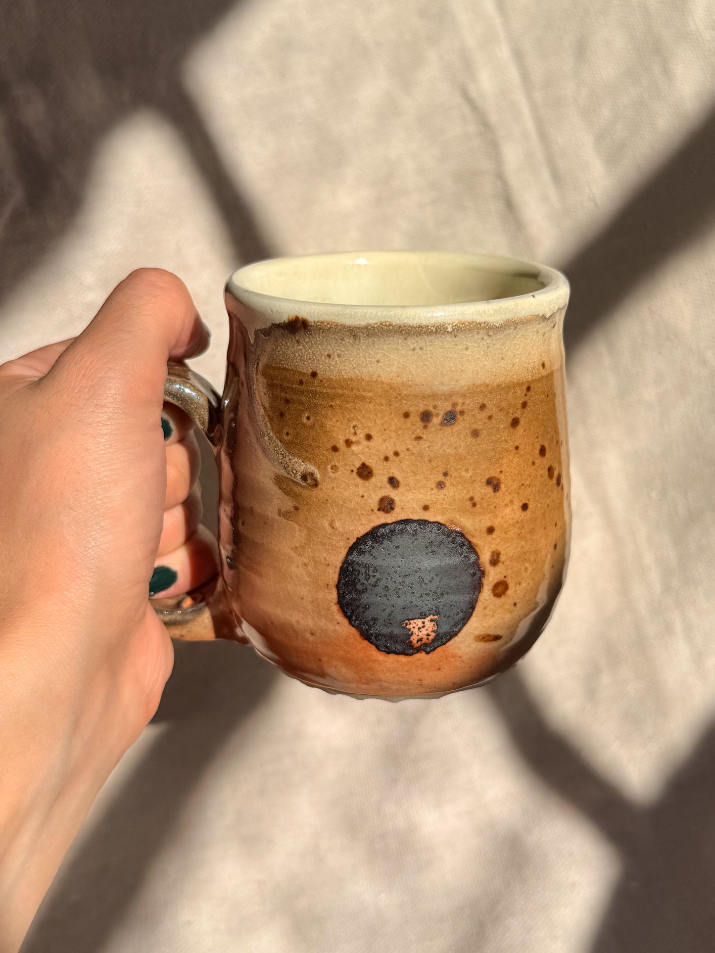 Hand holding a ceramic mug with speckled design against a neutral background