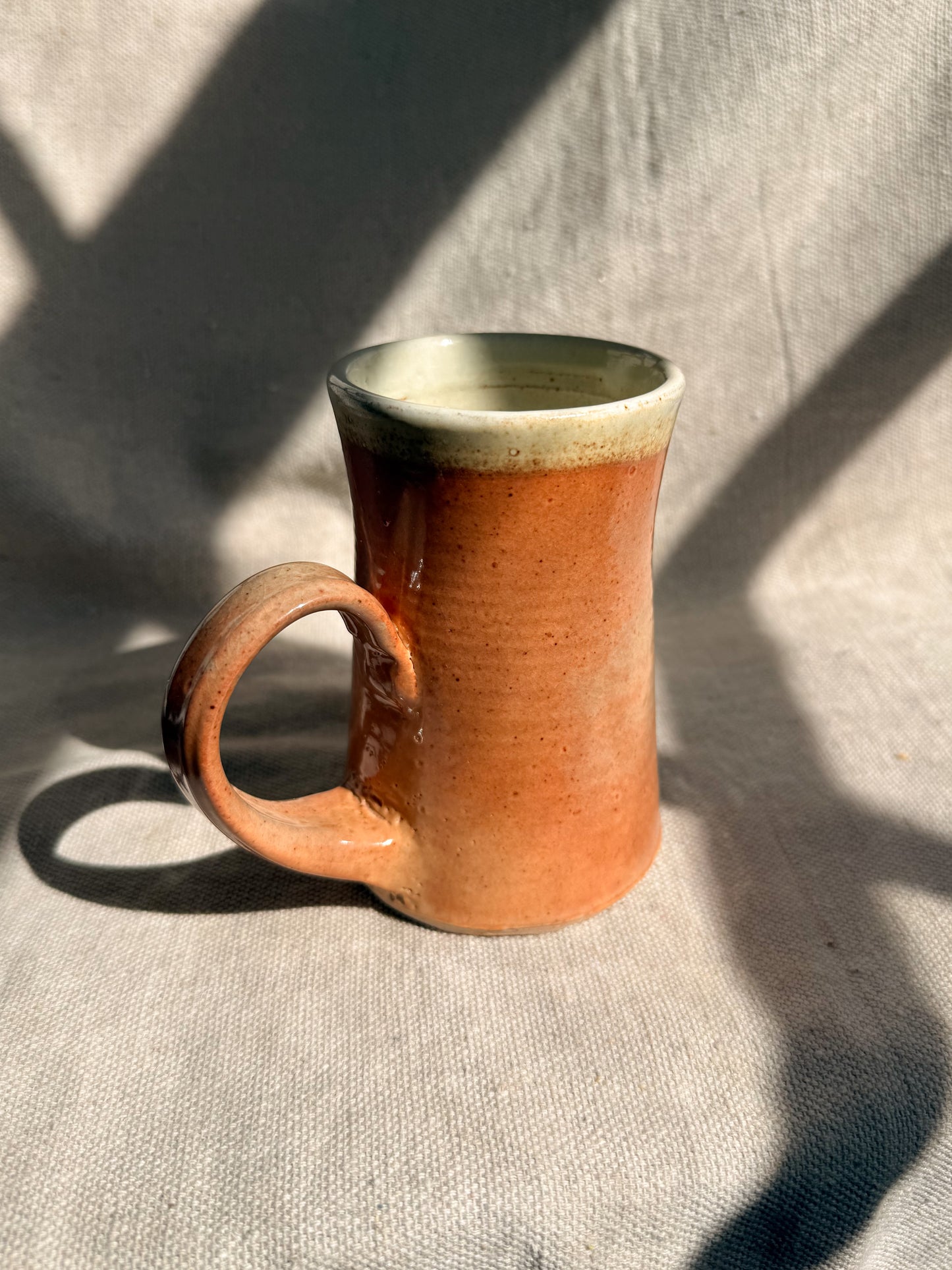 Ceramic mug with a brown body and green rim on a textured surface