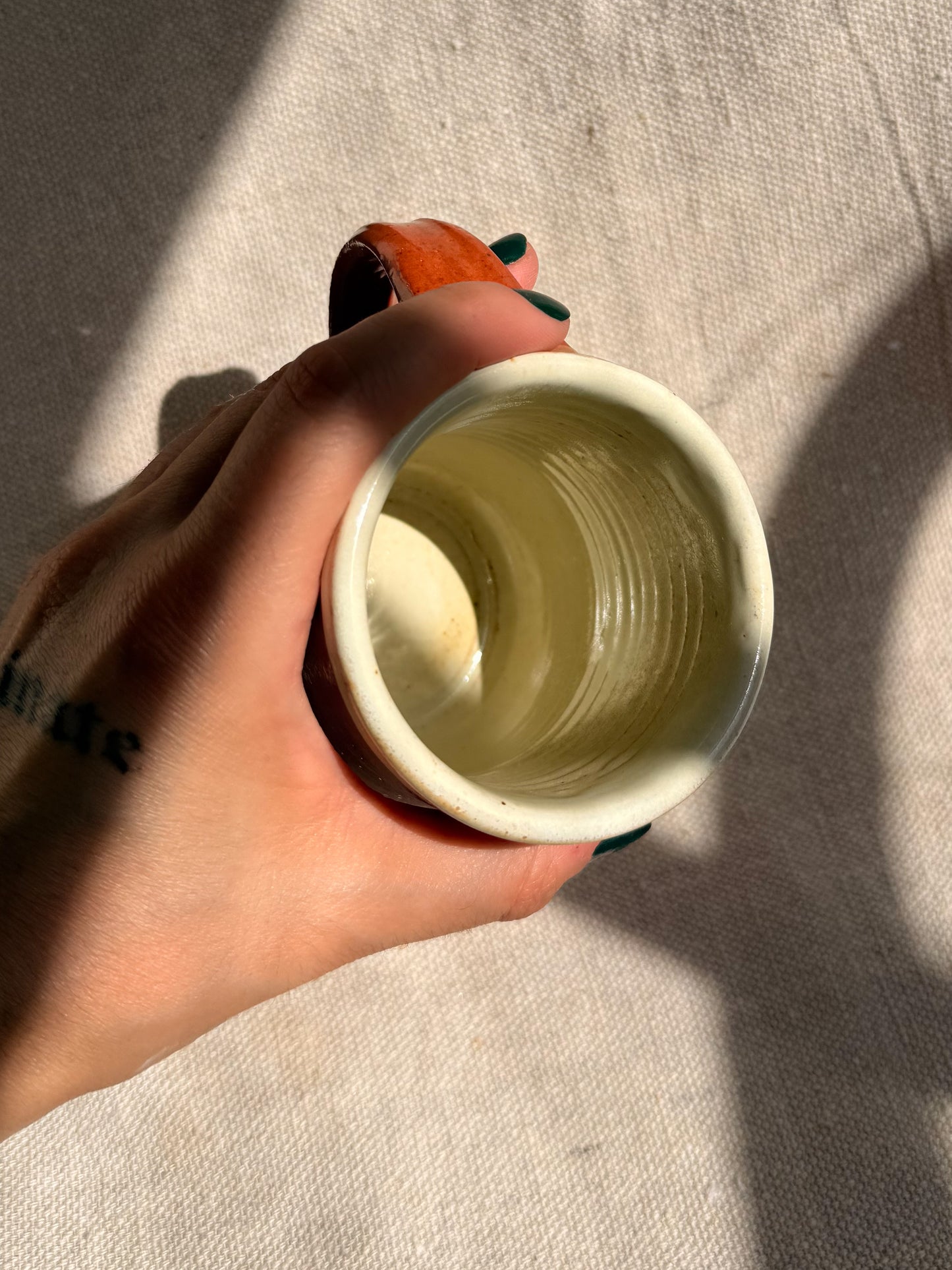 Hand holding a small ceramic cup against a neutral background