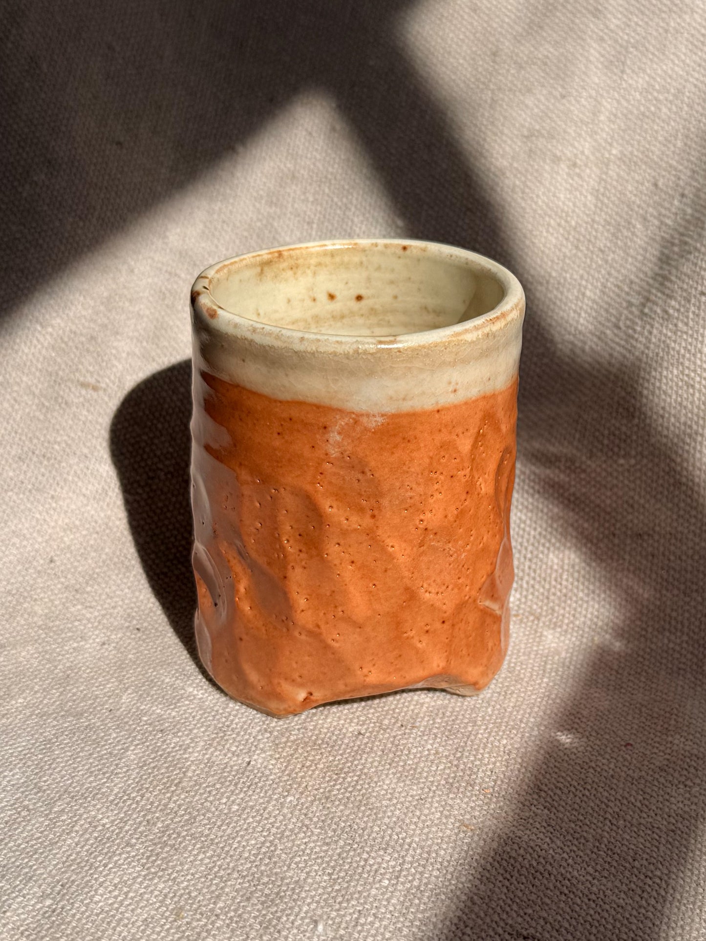 Small ceramic cup with a textured surface on a textured fabric background