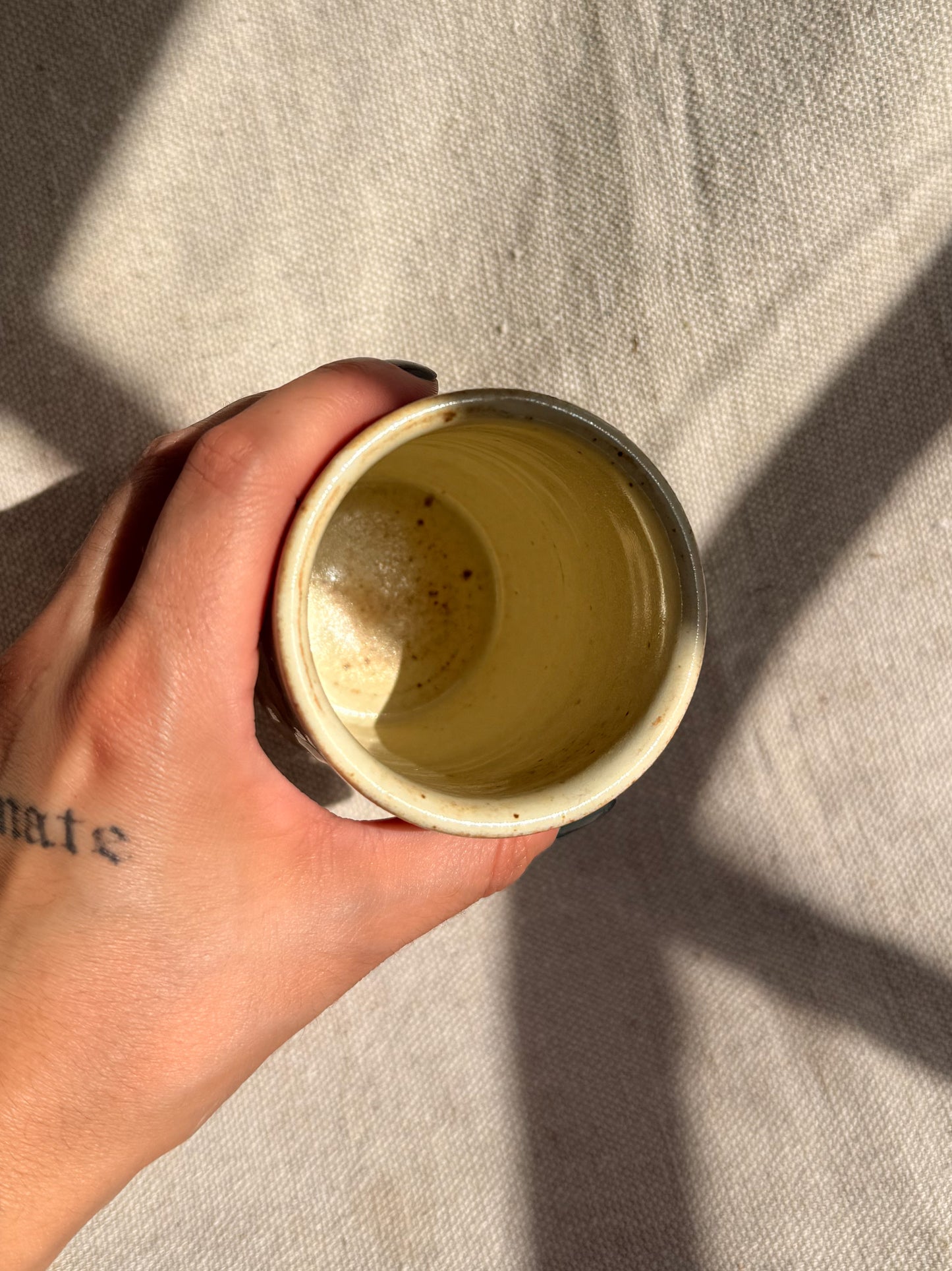 Hand holding a small ceramic cup against a neutral background