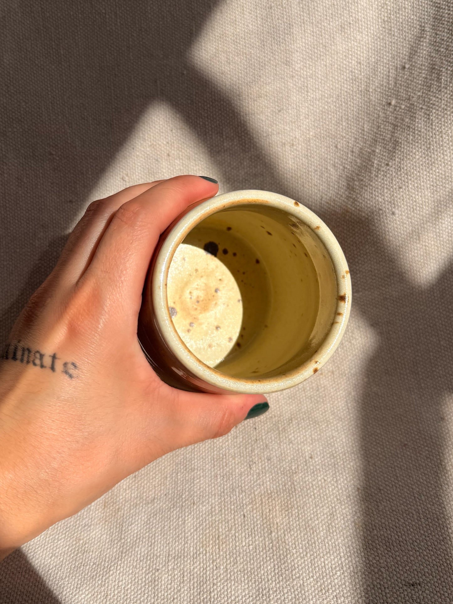 Hand holding a small ceramic cup with a textured interior against a neutral background