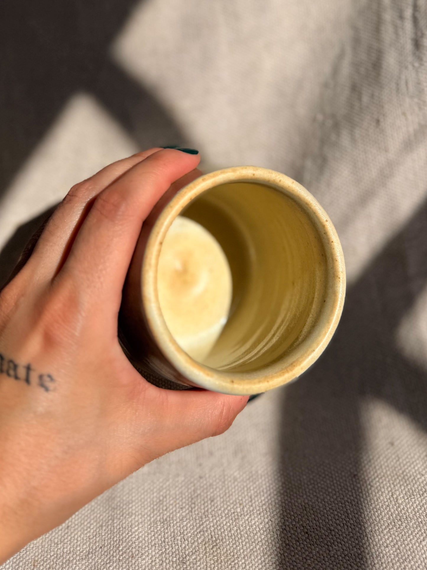 Hand holding a cylindrical beige object against a neutral background