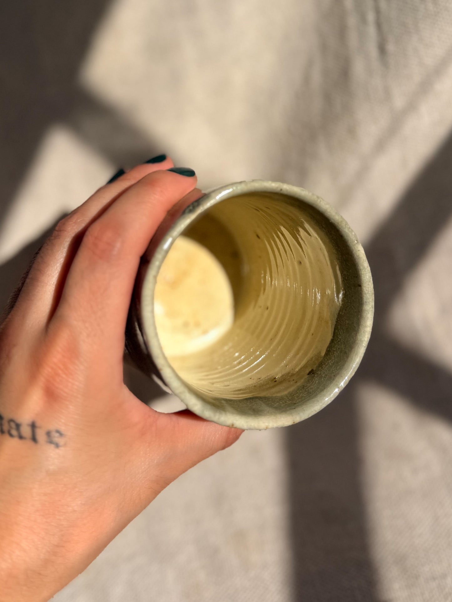 Hand holding a small ceramic cup with a textured interior against a neutral background