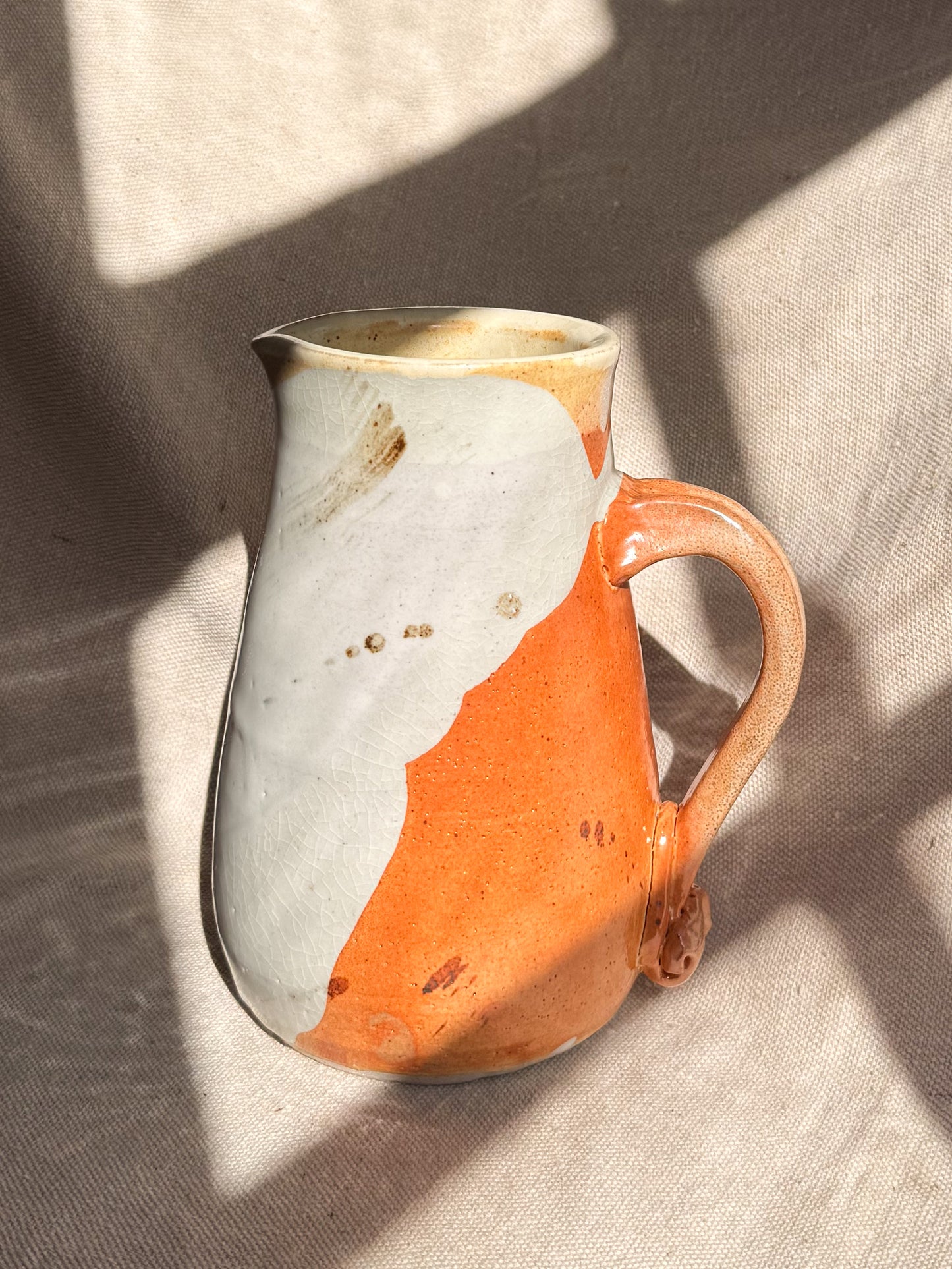 Ceramic pitcher with orange and white design on a textured surface