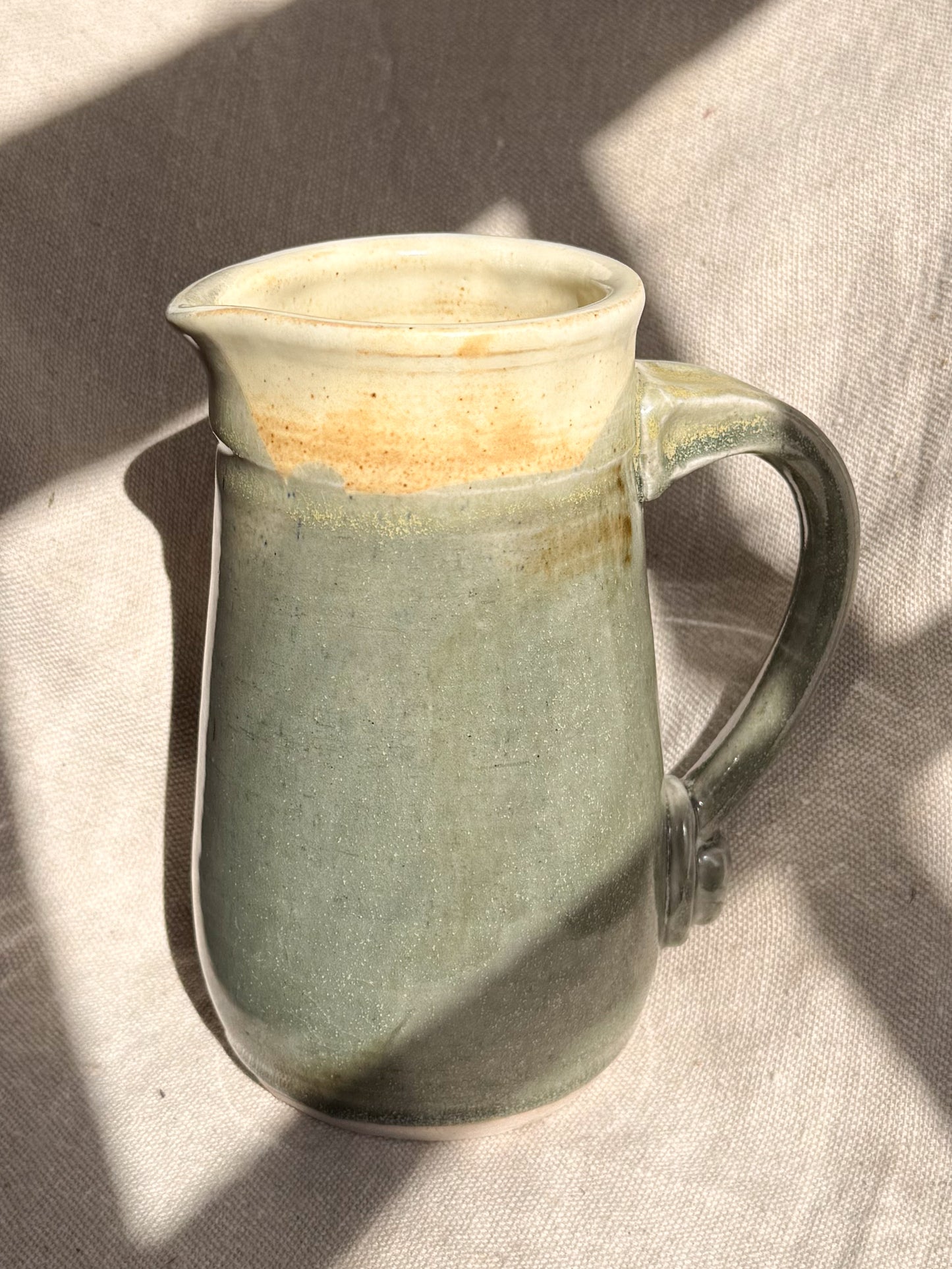 Green ceramic pitcher with a handle on a textured surface