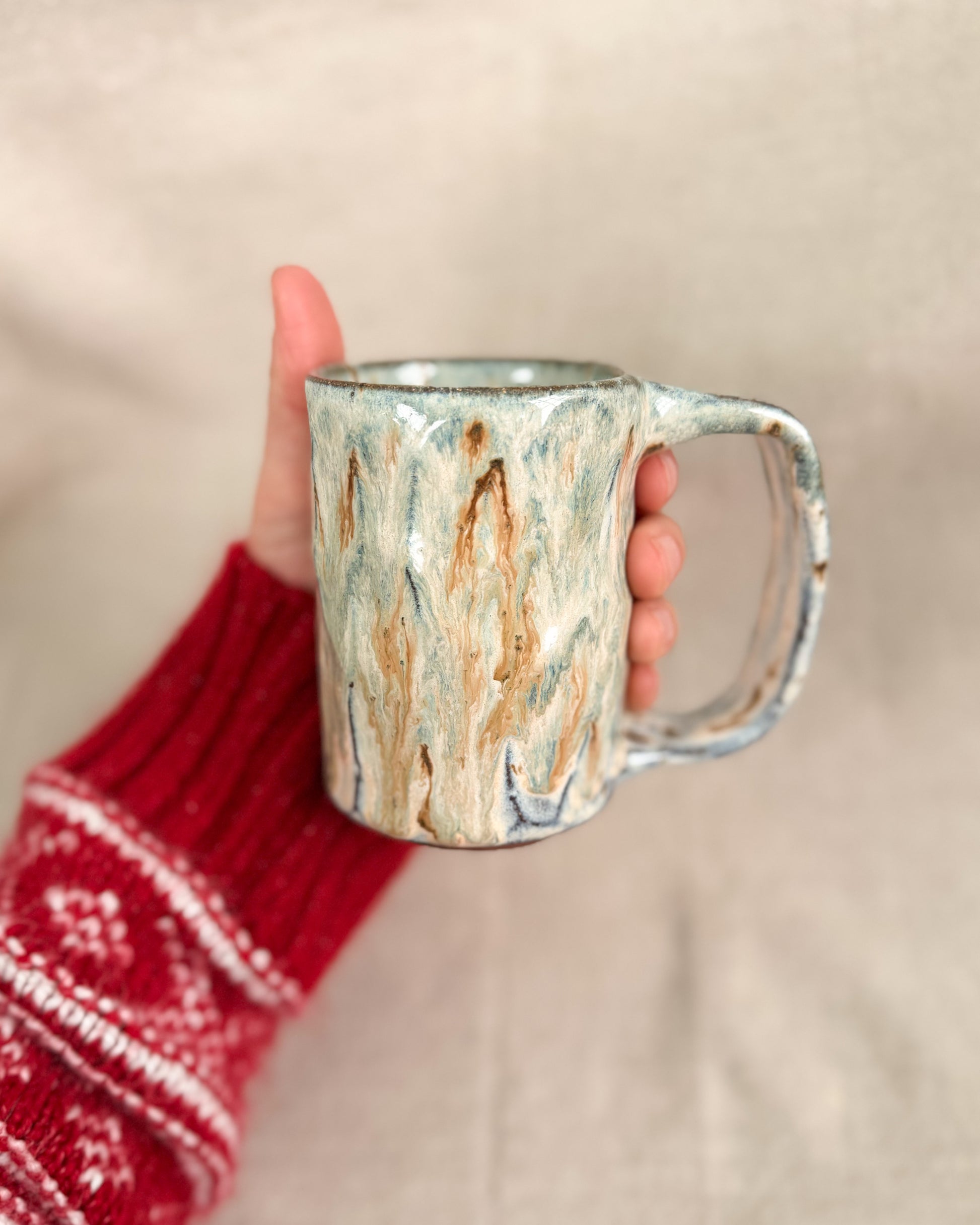 Hand holding a ceramic mug with a marbled design against a neutral background