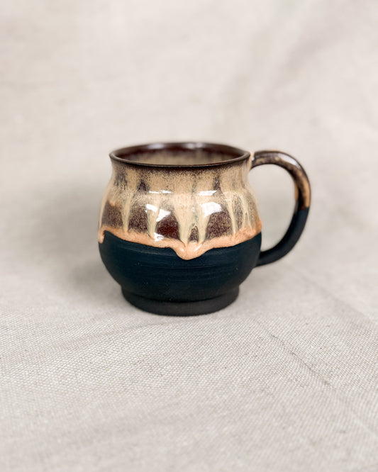 Ceramic mug with gold and black design on a beige background