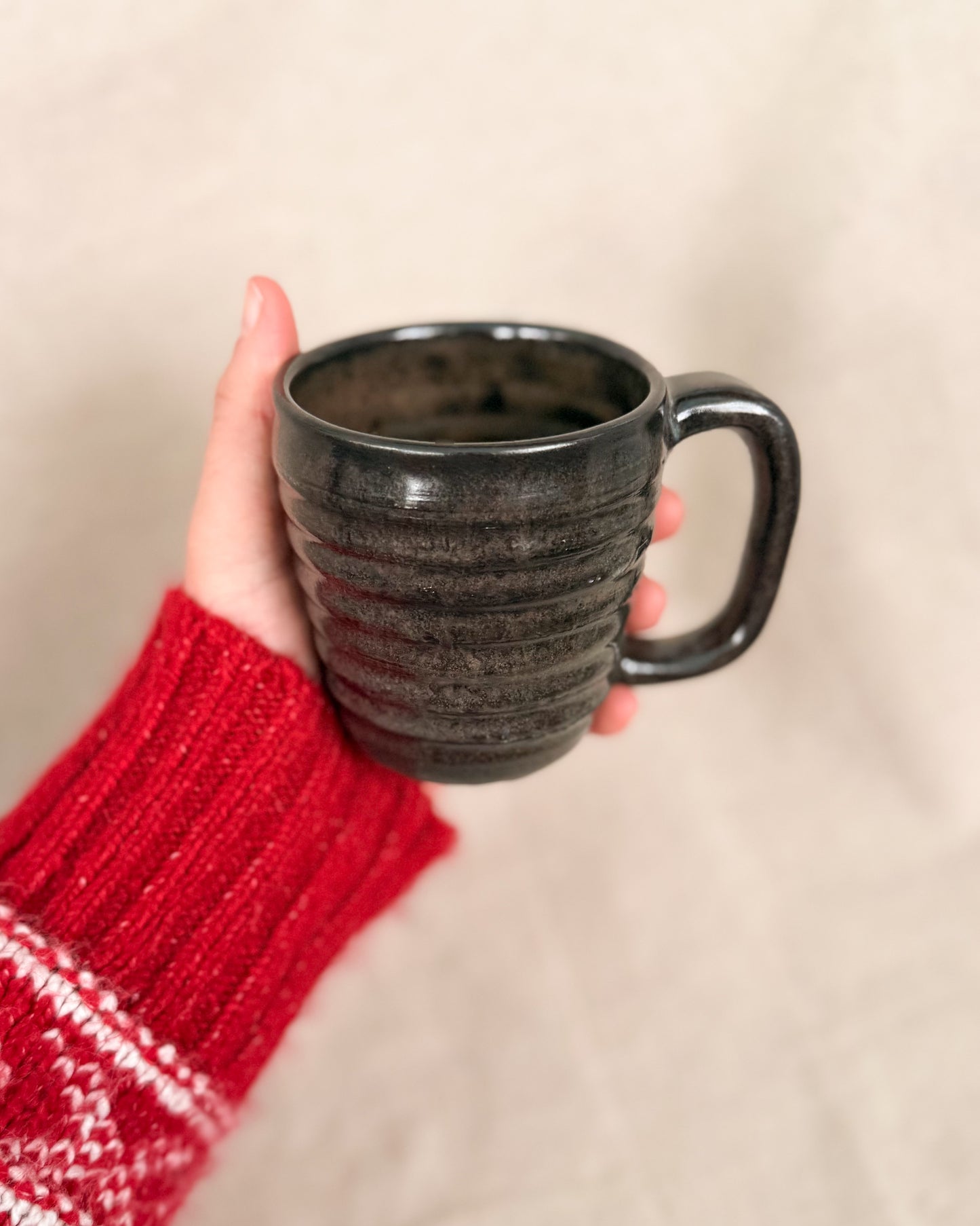Hand holding a black textured mug with a red sleeve against a beige background