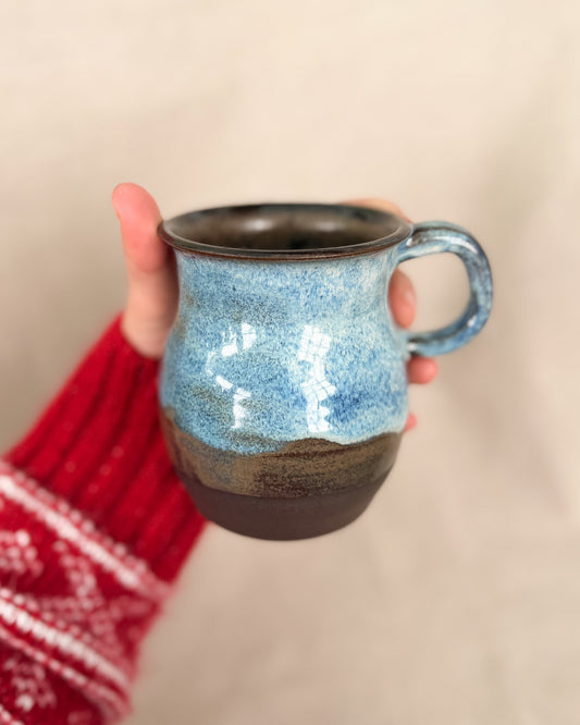 Hand holding a blue speckled ceramic mug with a brown base against a beige background
