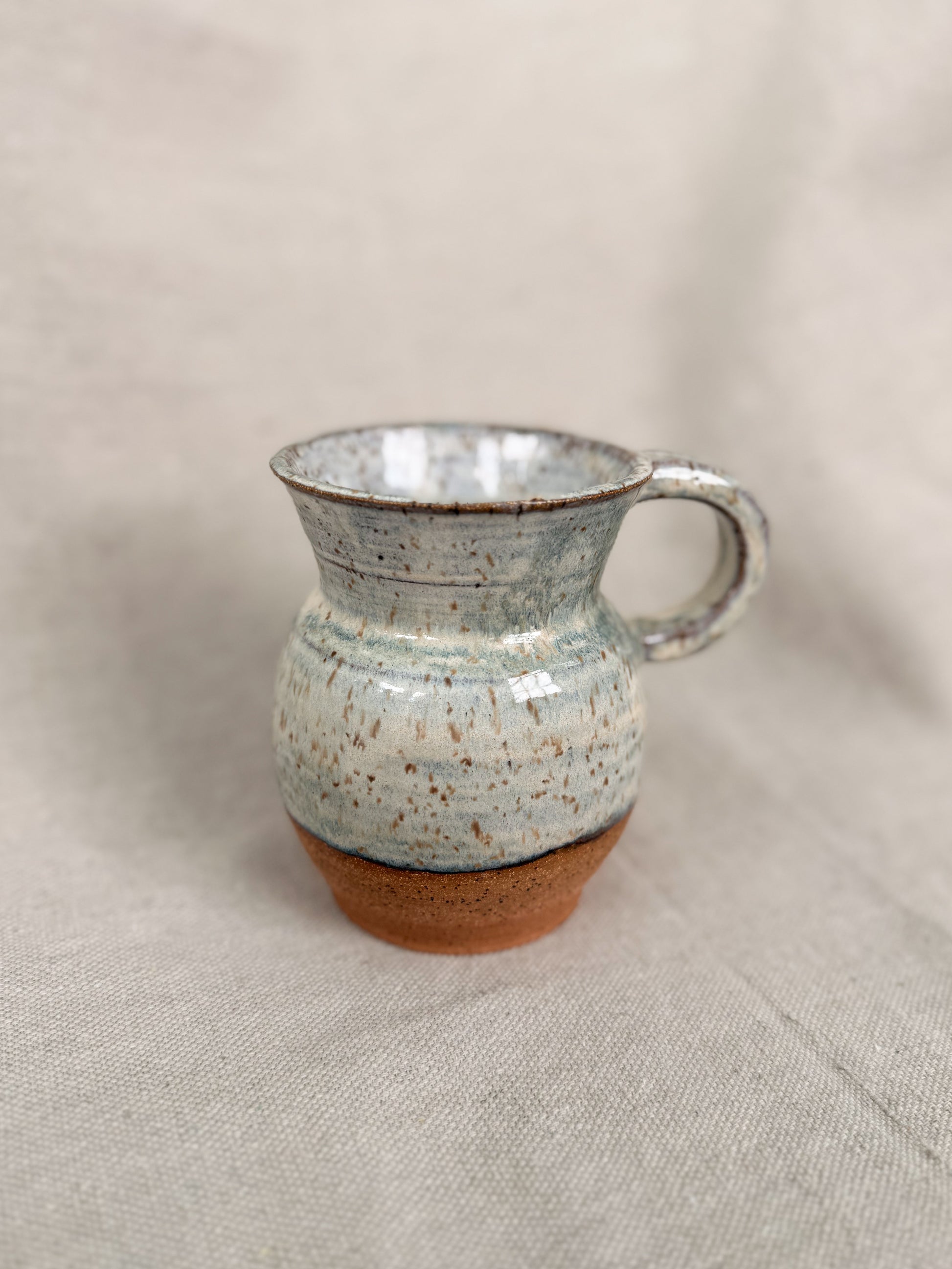 Ceramic mug with speckled glaze on a beige fabric background