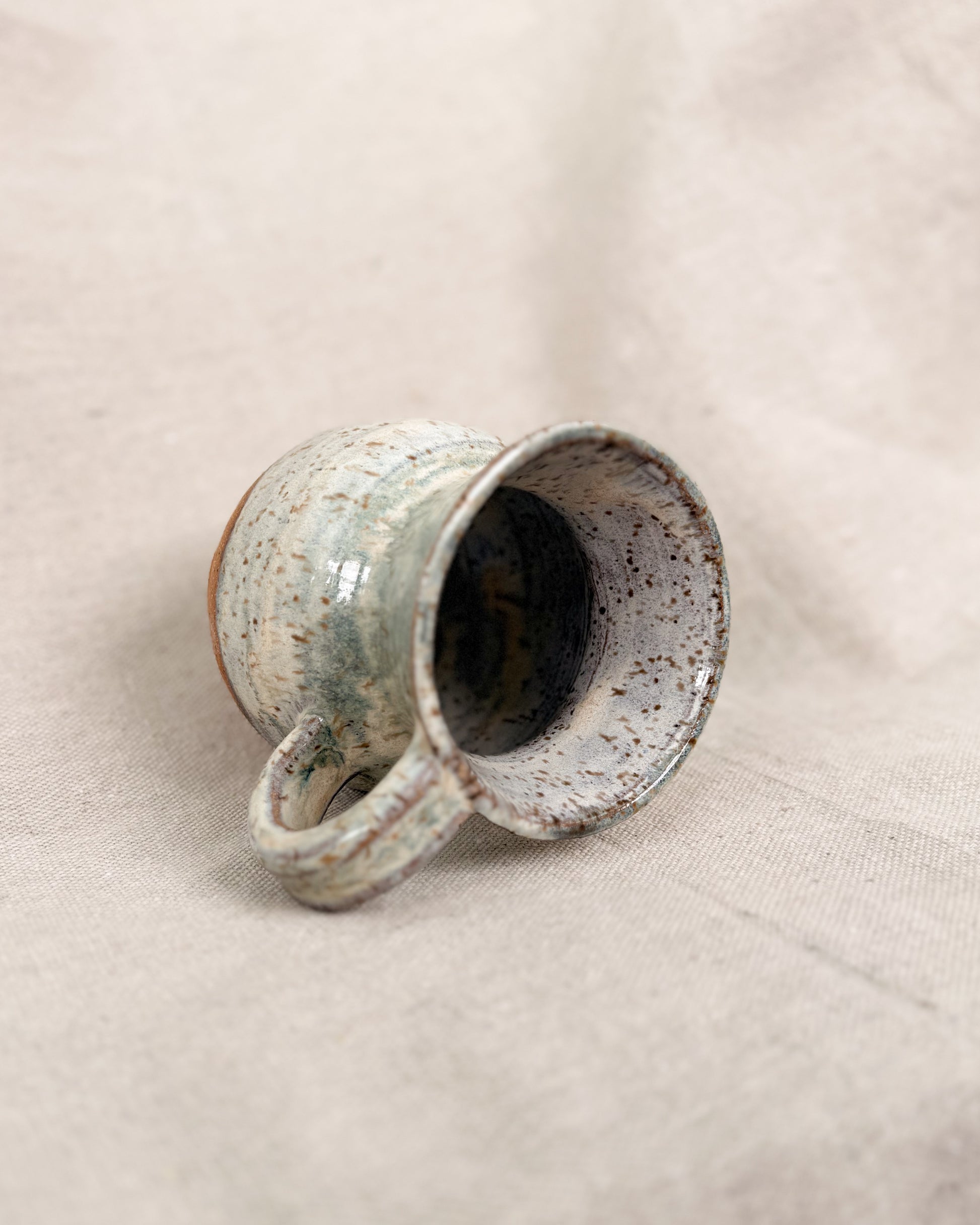 Speckled ceramic mug on a beige fabric background