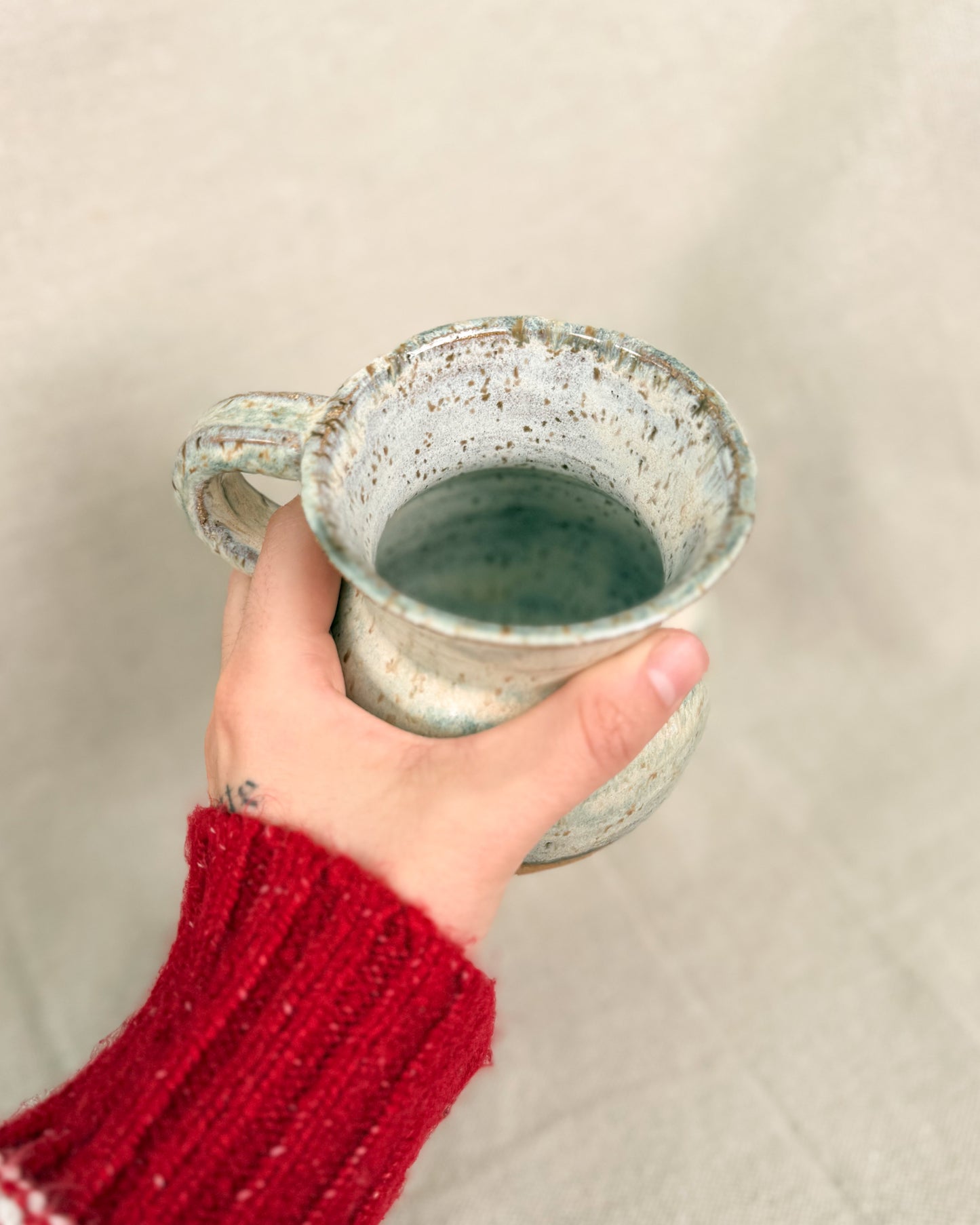 Hand holding a ceramic mug with a speckled design against a plain background