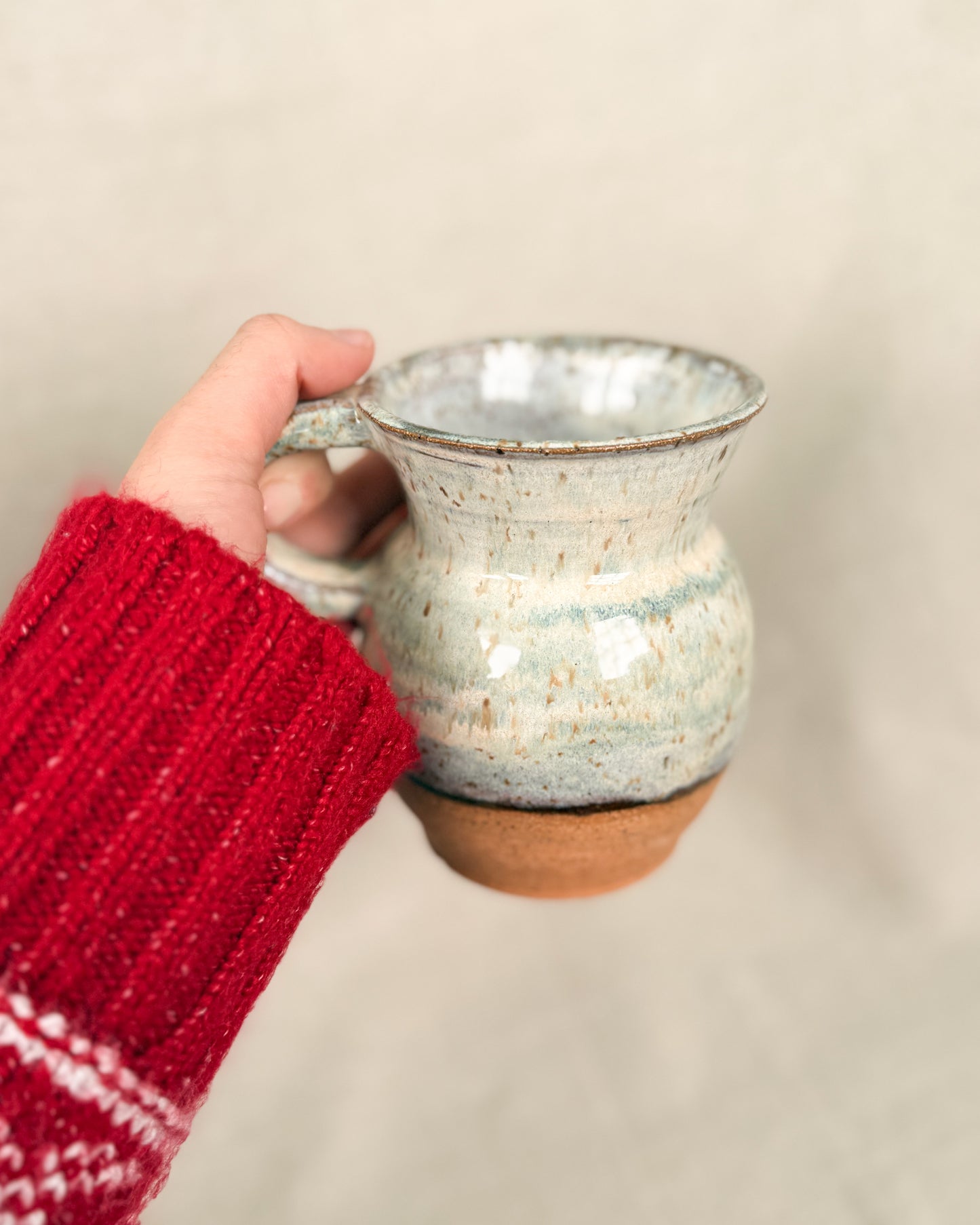 Hand holding a ceramic mug with a red sleeve against a beige background