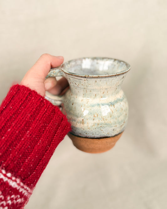 Hand holding a ceramic mug with a red sleeve against a beige background