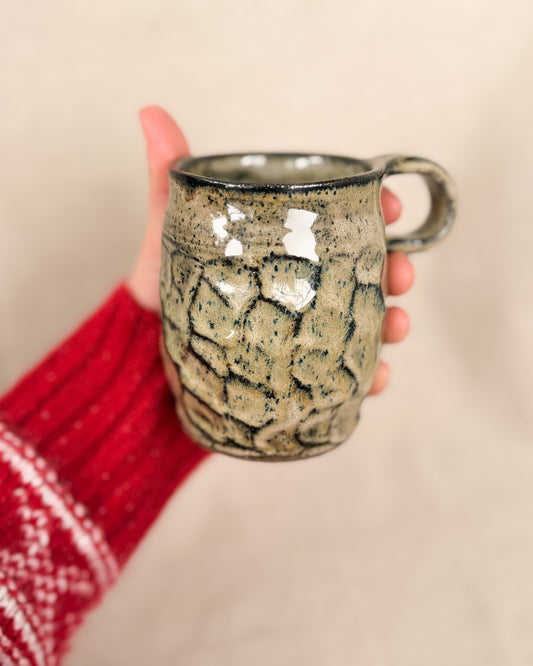 Hand holding a ceramic mug with a textured surface against a neutral background