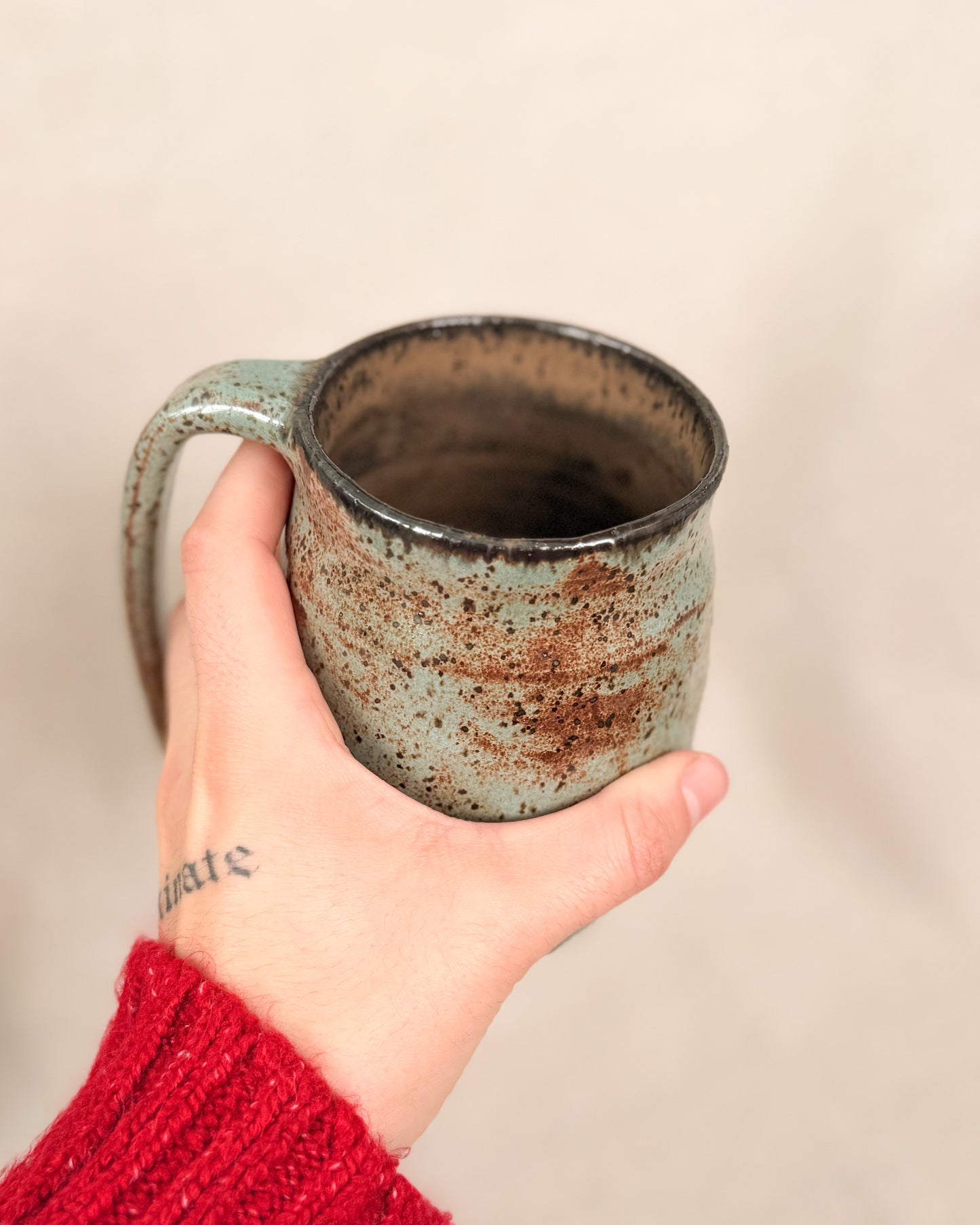 Hand holding a rustic ceramic mug with a beige background
