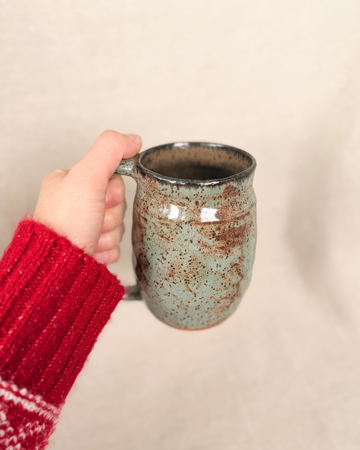 Hand holding a ceramic mug with a speckled design against a beige background