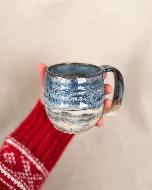 Hand holding a blue ceramic mug with a textured surface against a neutral background