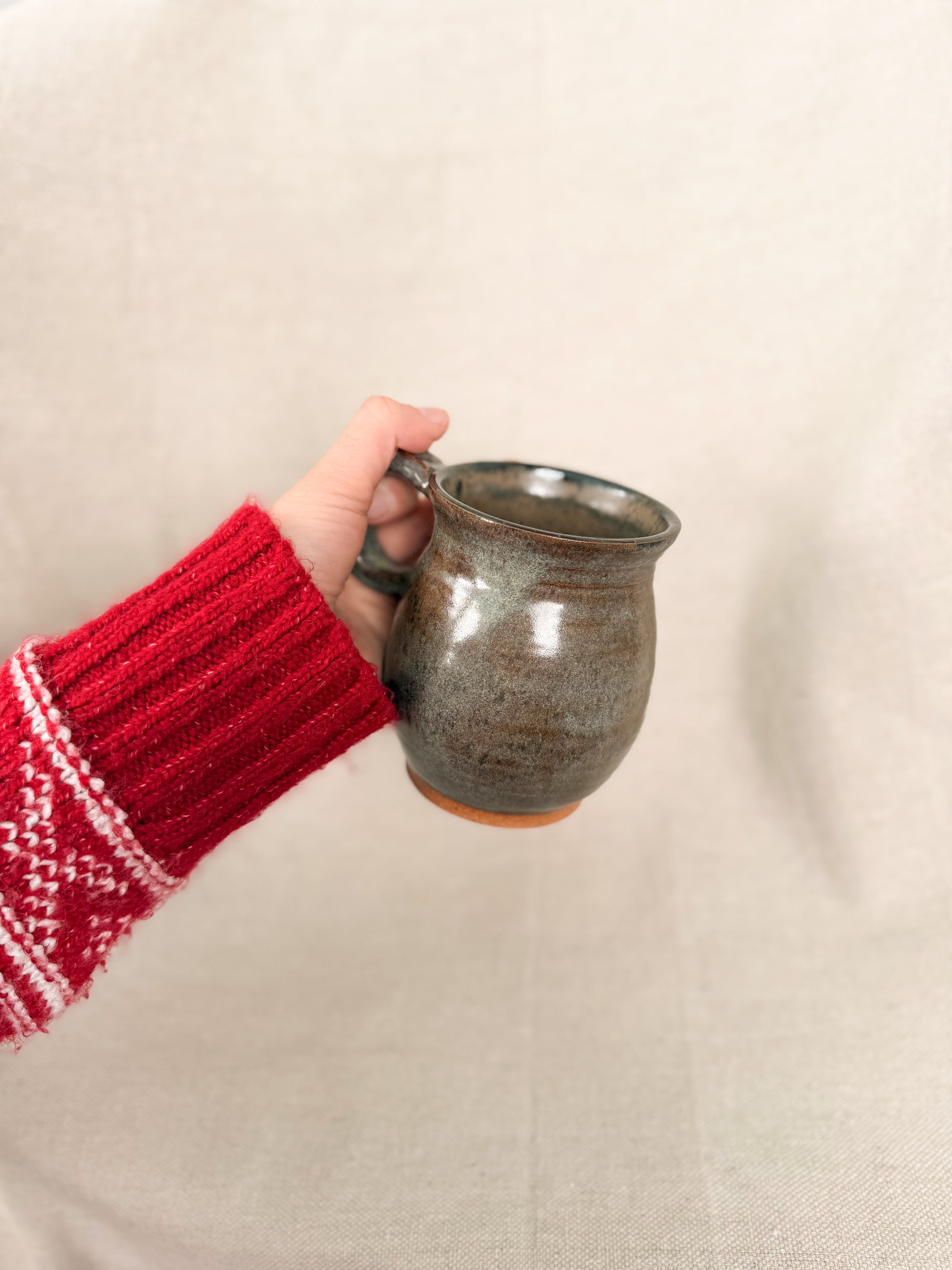 Hand holding a ceramic mug with a red sleeve against a beige background