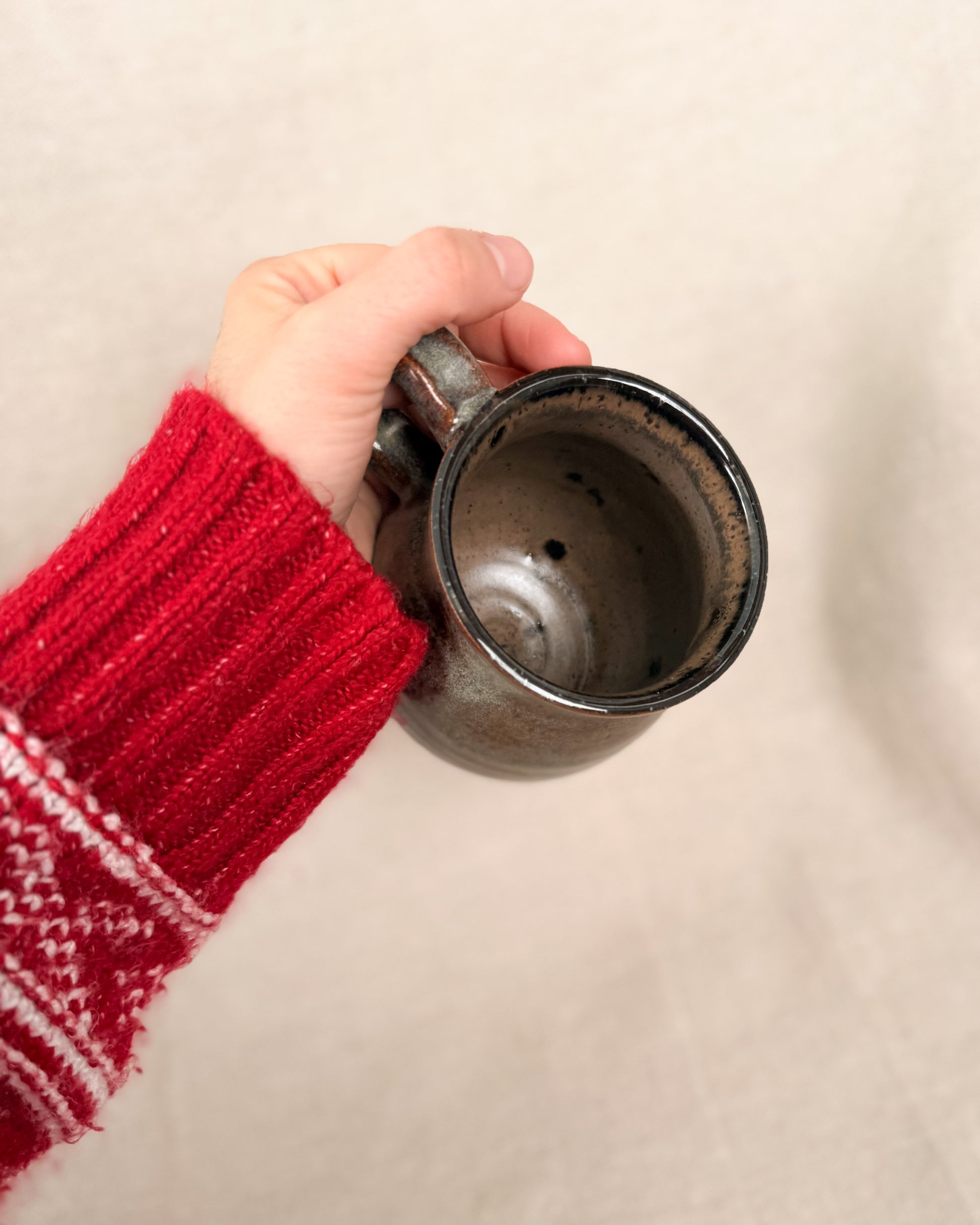 Hand holding a mug with a red sleeve on a beige background