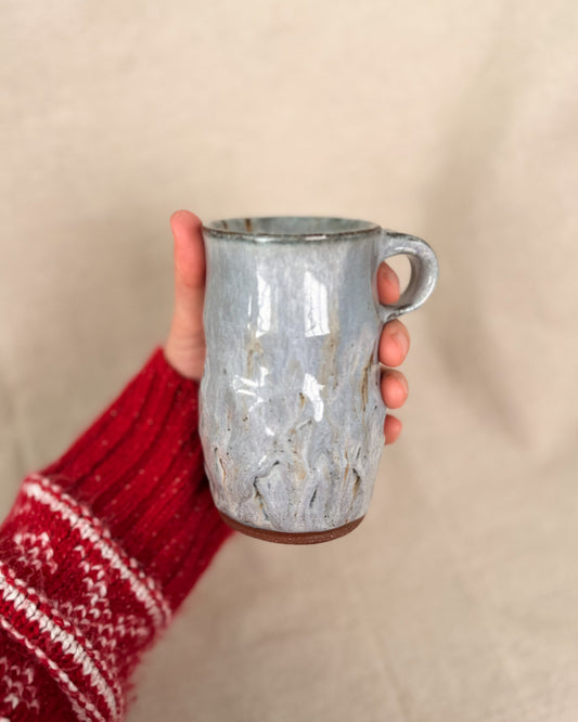 Hand holding a textured ceramic mug against a beige background