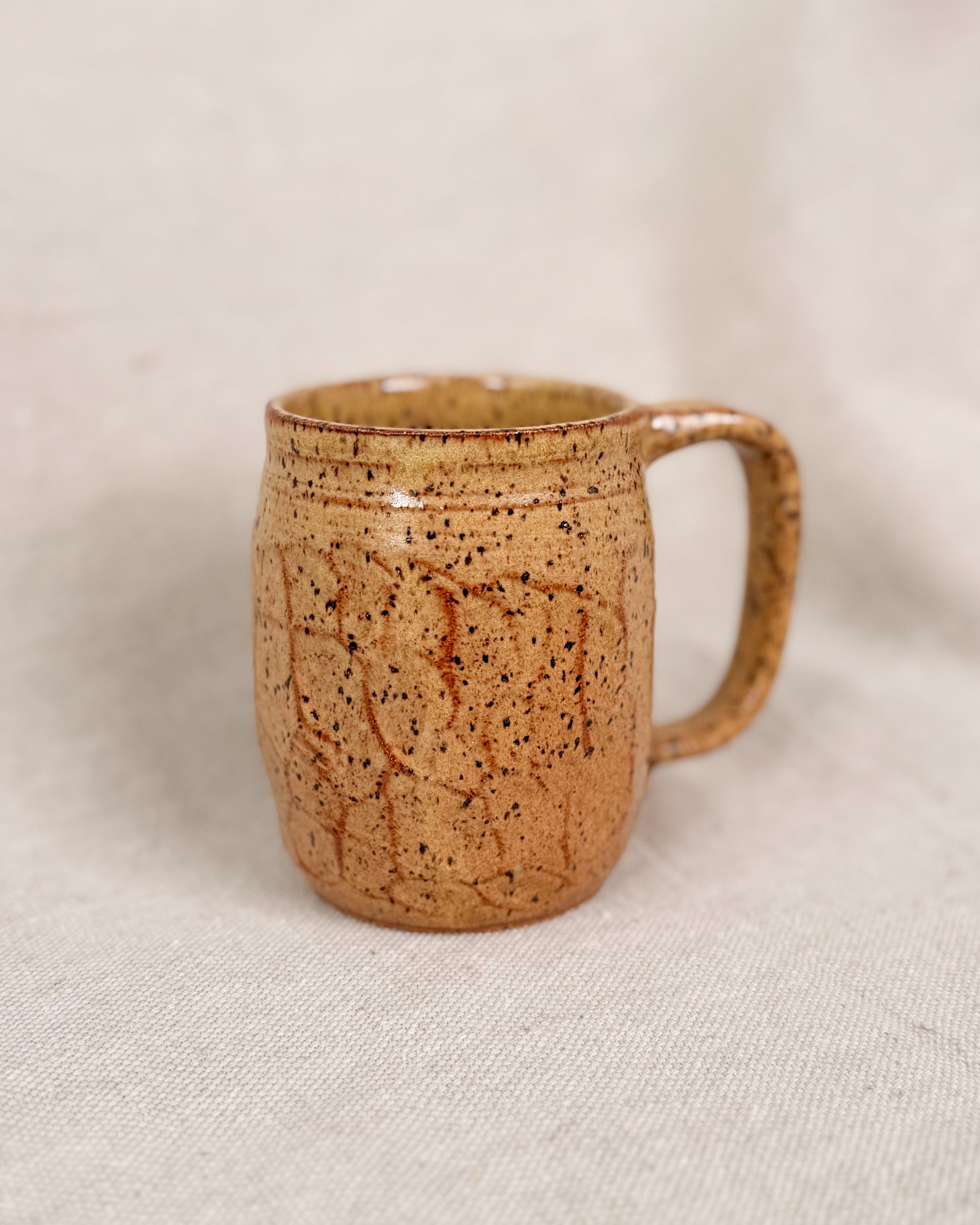 Brown speckled ceramic mug on a beige fabric background