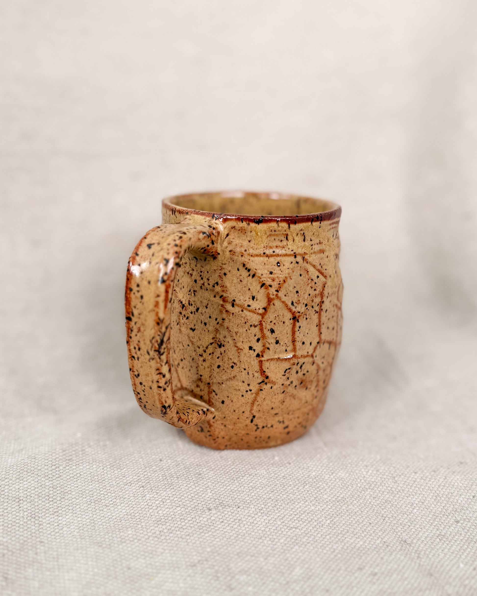 Brown ceramic mug with speckled pattern on a light beige background