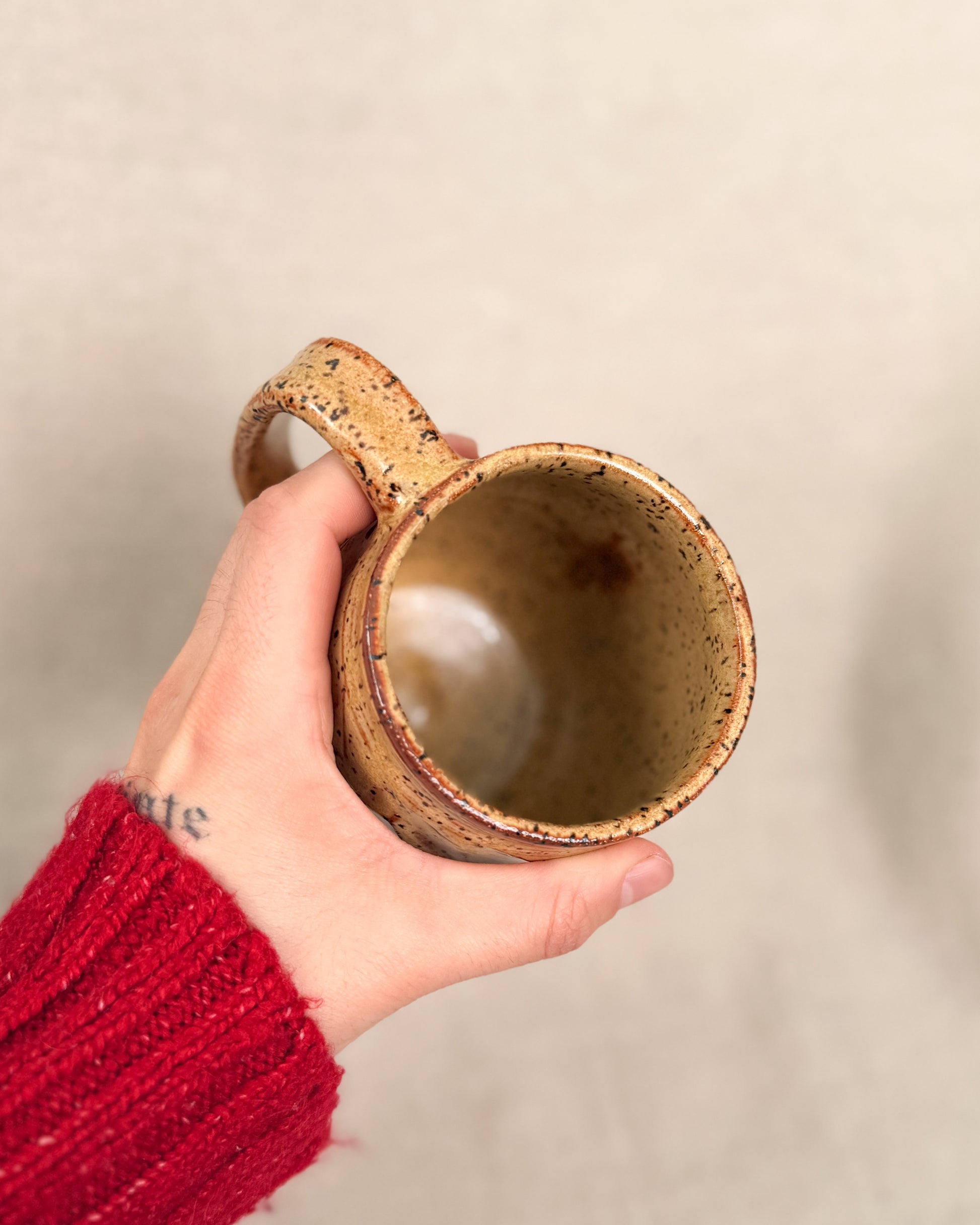 Hand holding a ceramic mug with a textured surface against a plain background