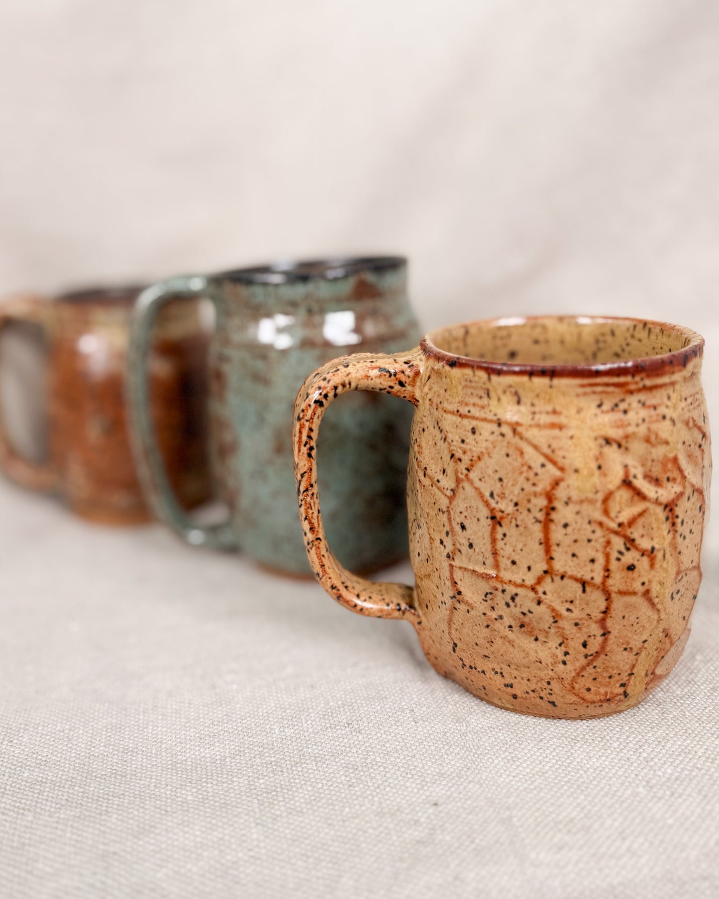 Three ceramic mugs with textured surfaces on a light fabric background
