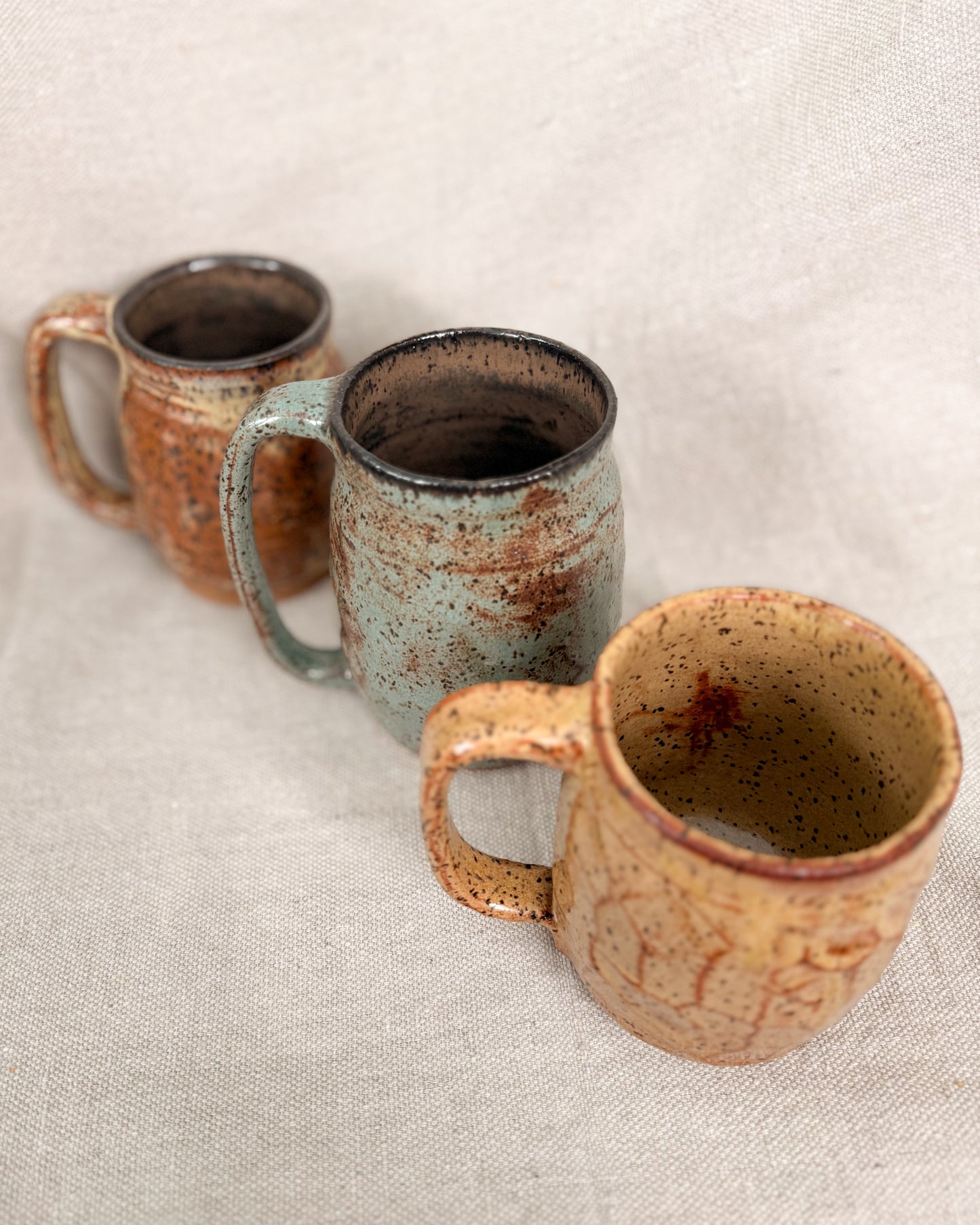 Three ceramic mugs with rustic finishes on a textured surface