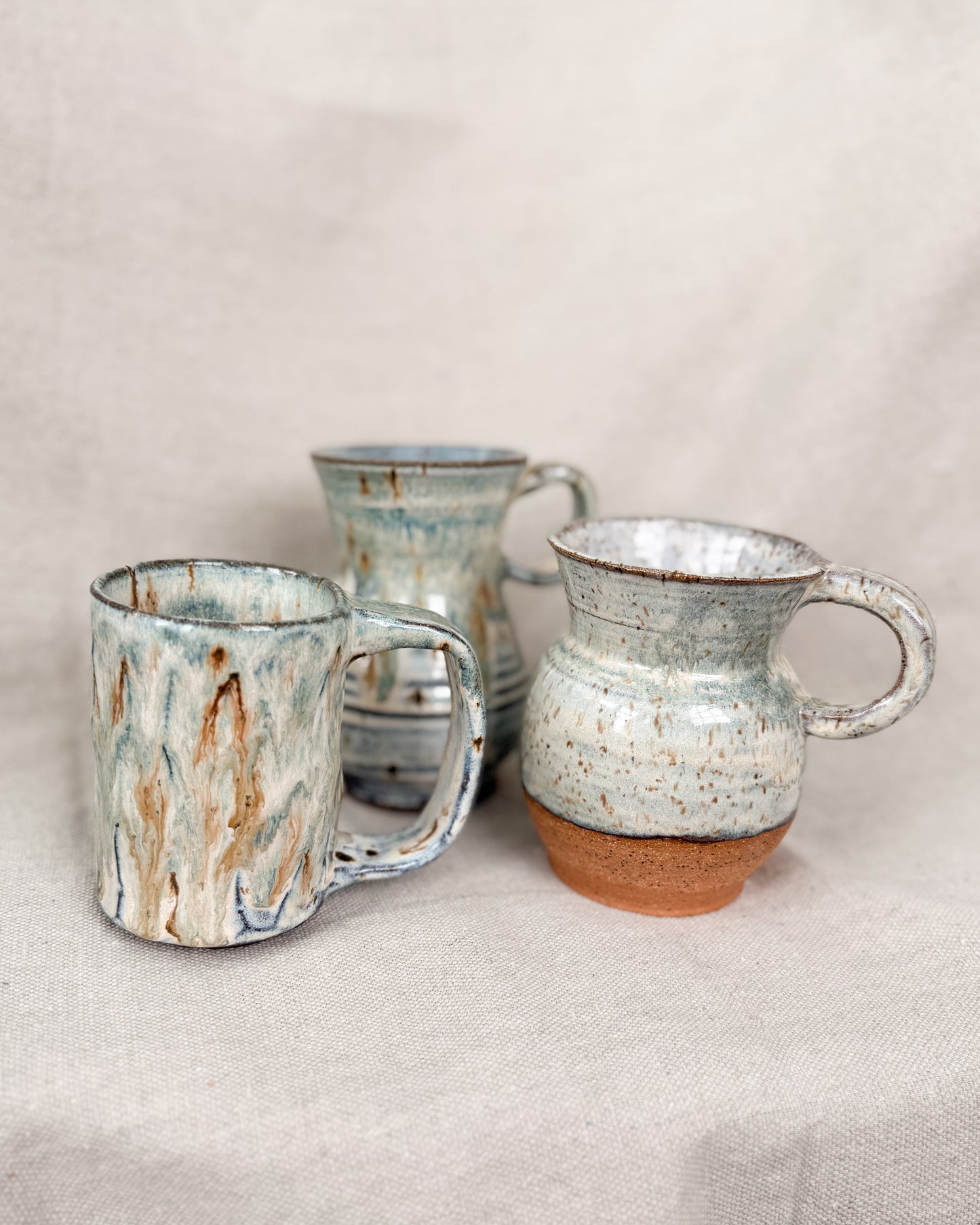 Three ceramic mugs with rustic textures on a beige background