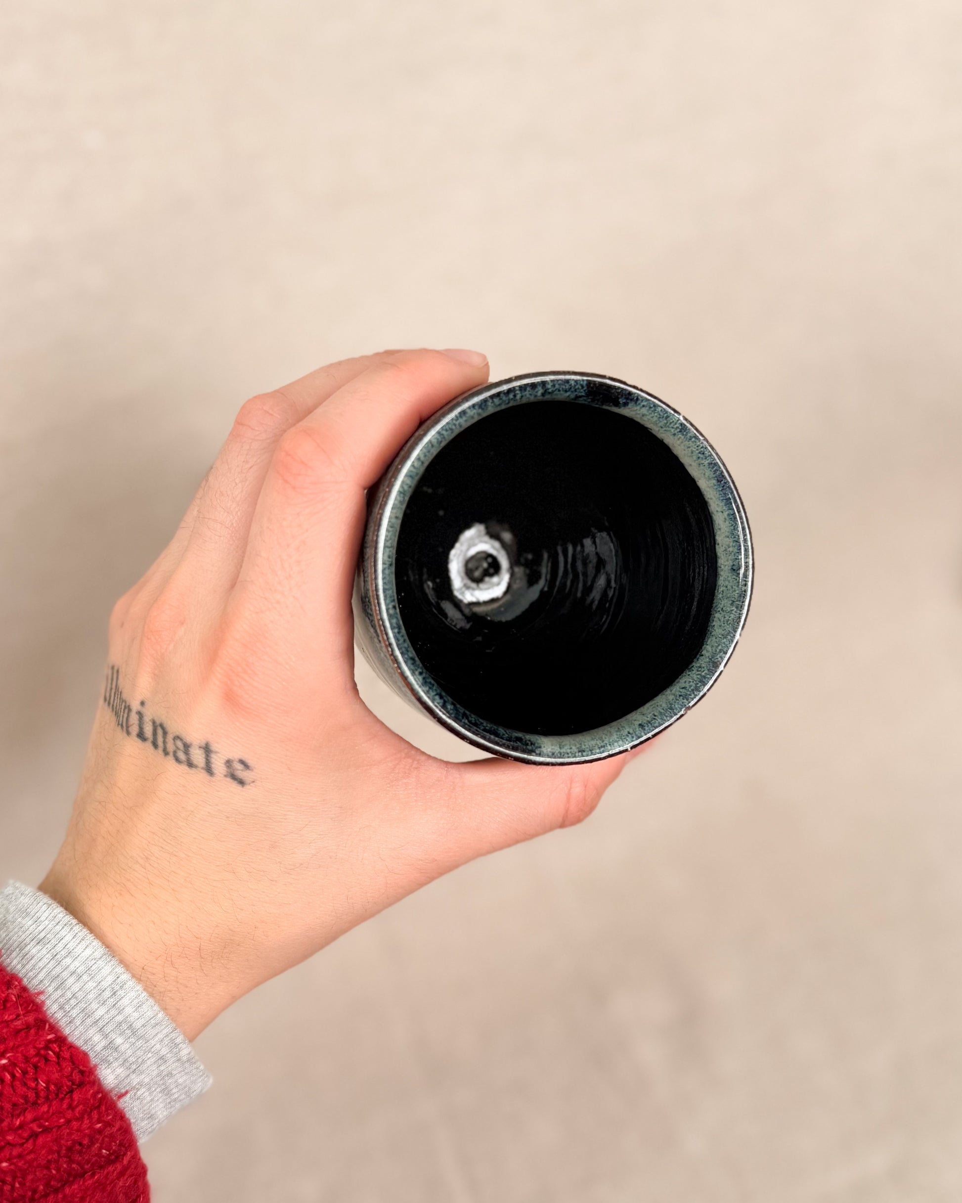 Hand holding a black cylindrical object against a beige background, 6 ounces