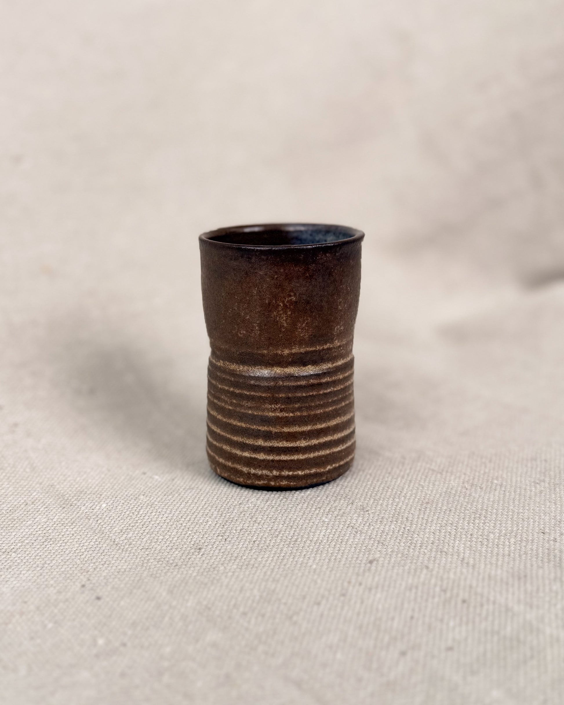 Brown ceramic cup with ribbed texture on a beige fabric background, 5 ounces