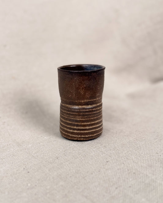 Brown ceramic cup with ribbed texture on a beige fabric background, 5 ounces