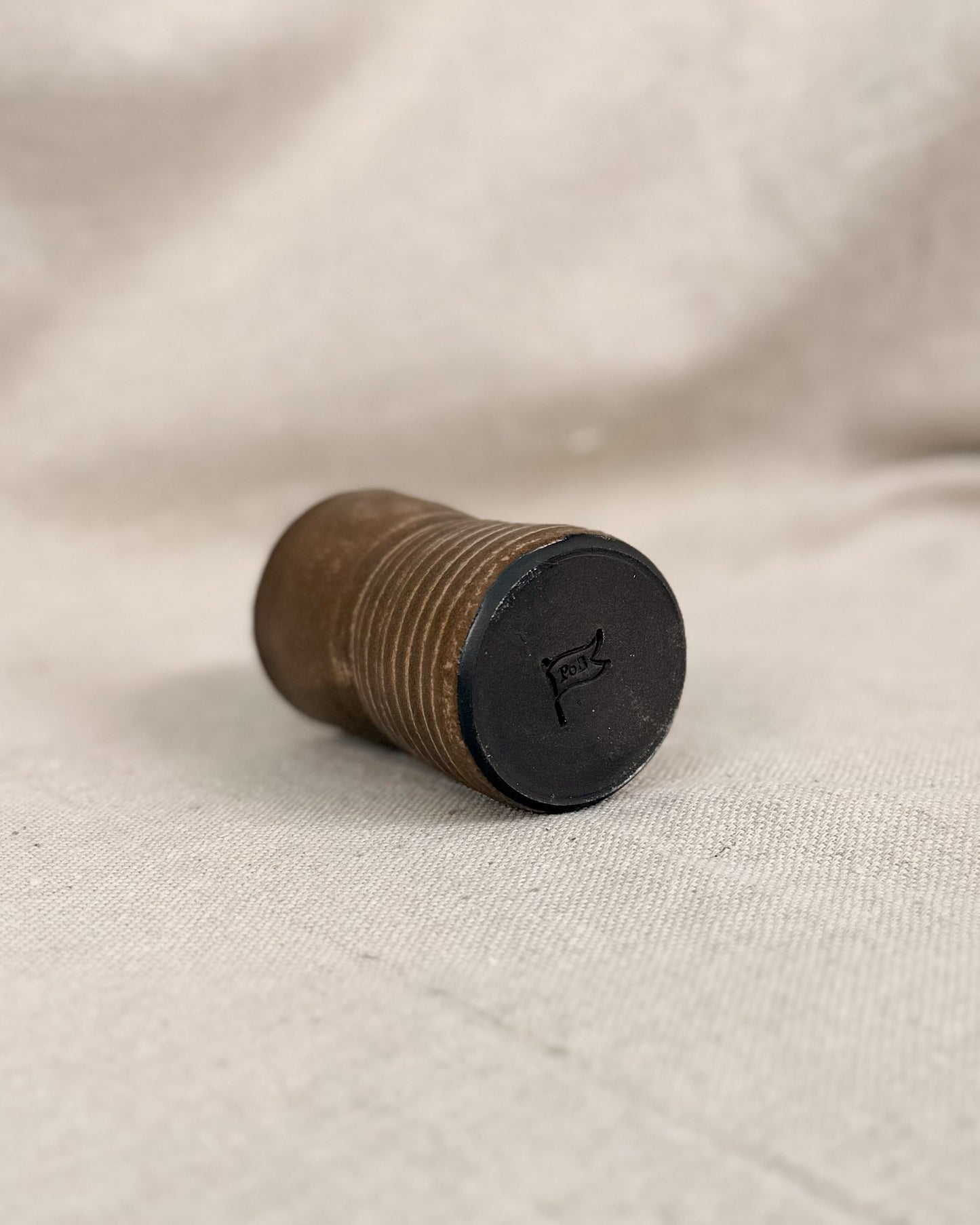 brown ceramic cup with a black bottom on a beige fabric background, 5 ounces