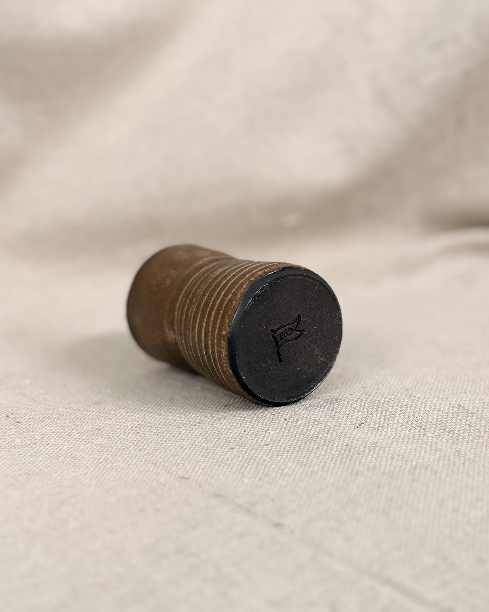 brown ceramic cup with a black bottom on a beige fabric background, 5 ounces