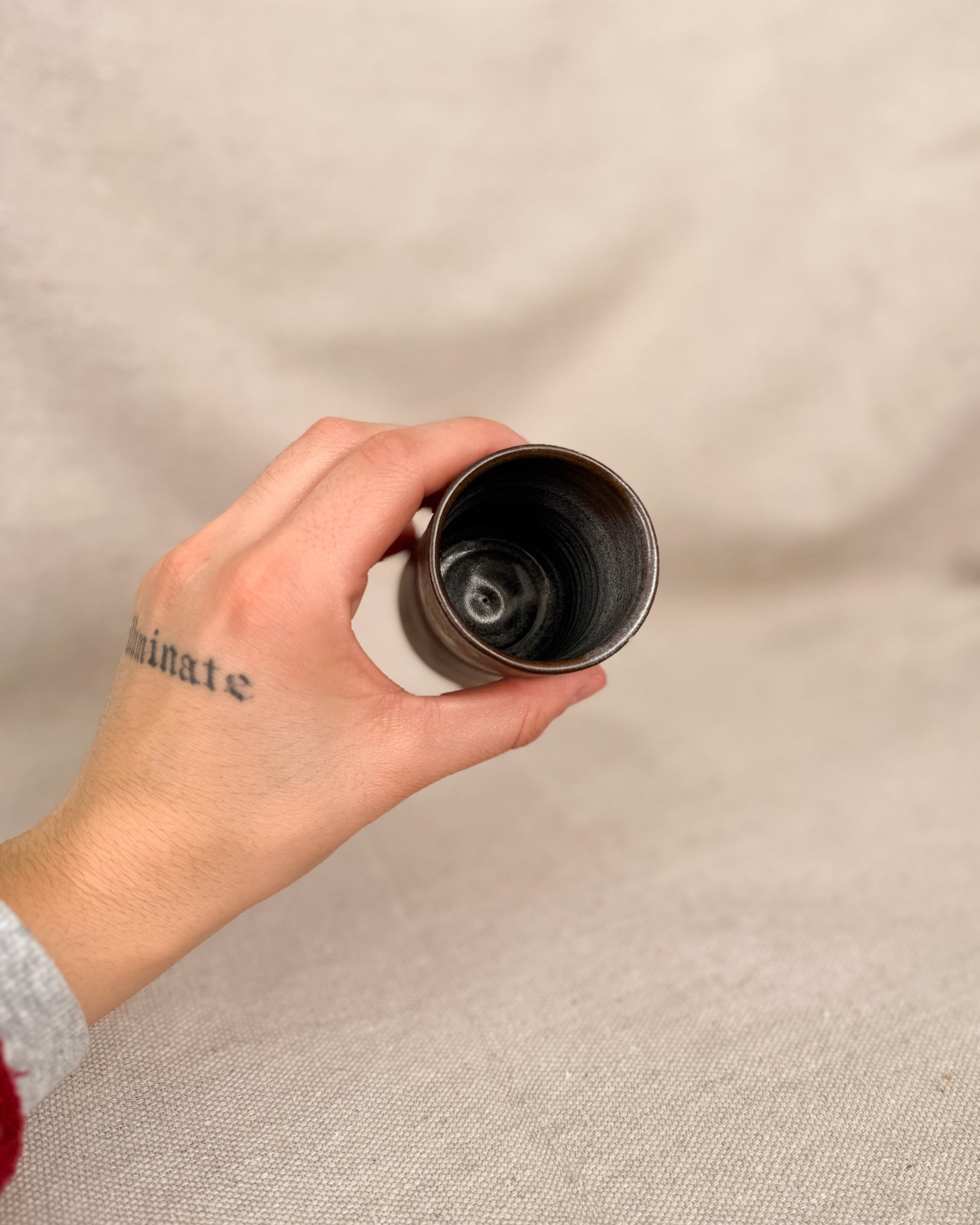 Hand holding a ceramic cup against a beige background, 5 ounces