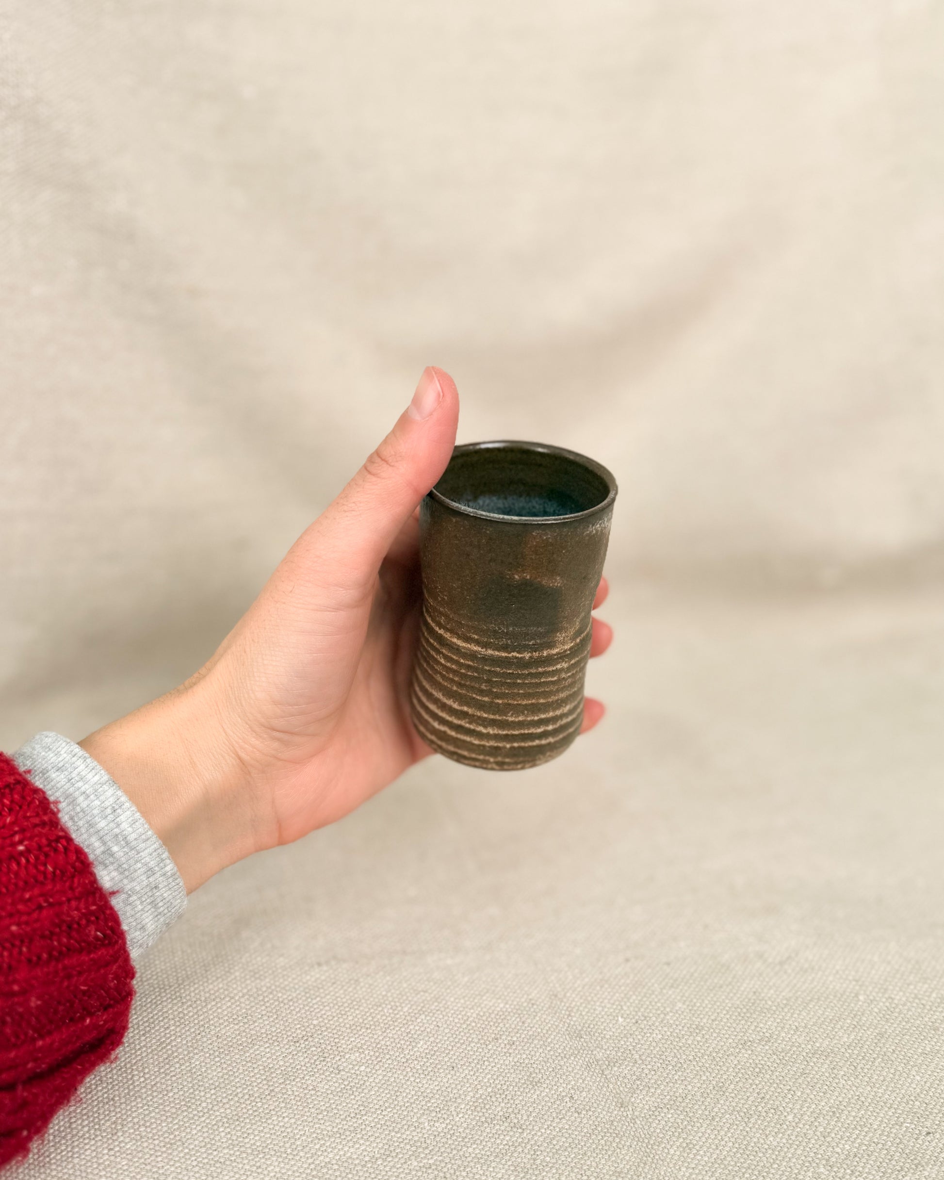 Hand holding a textured ceramic cup against a beige background, 5 ounces