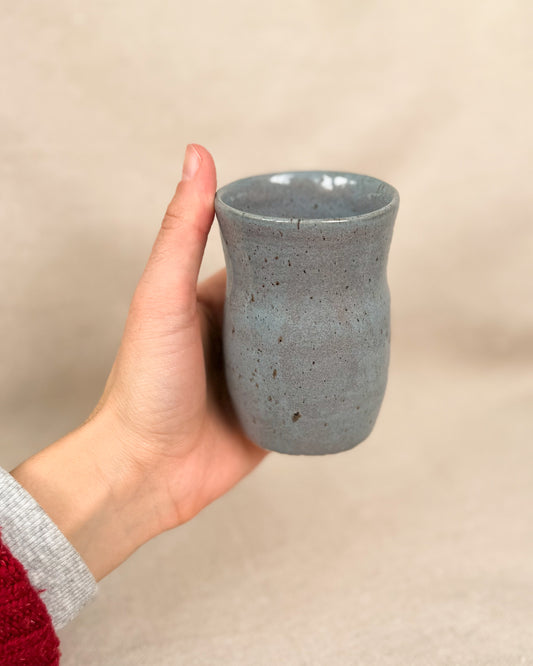 Hand holding a blue and gray ceramic cup against a beige background, 5 ounce capacity, 5 ounces