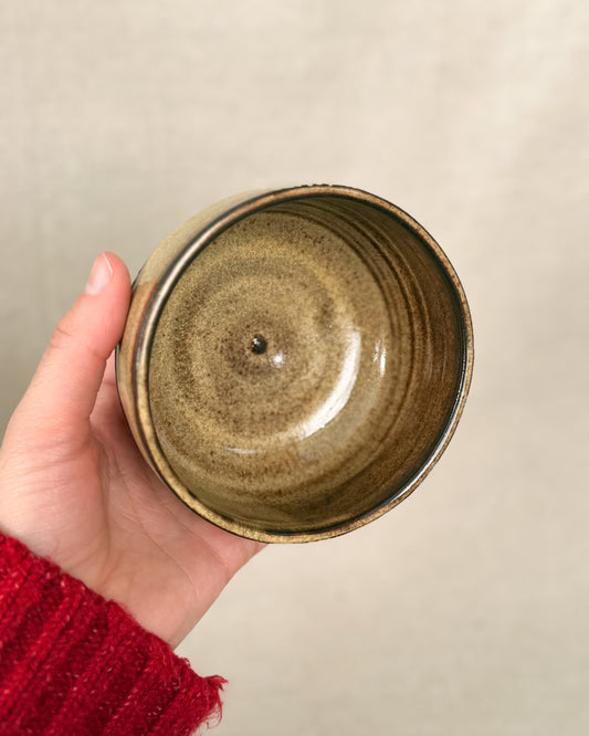 Hand holding a ceramic bowl with a beige background, 8 ounces