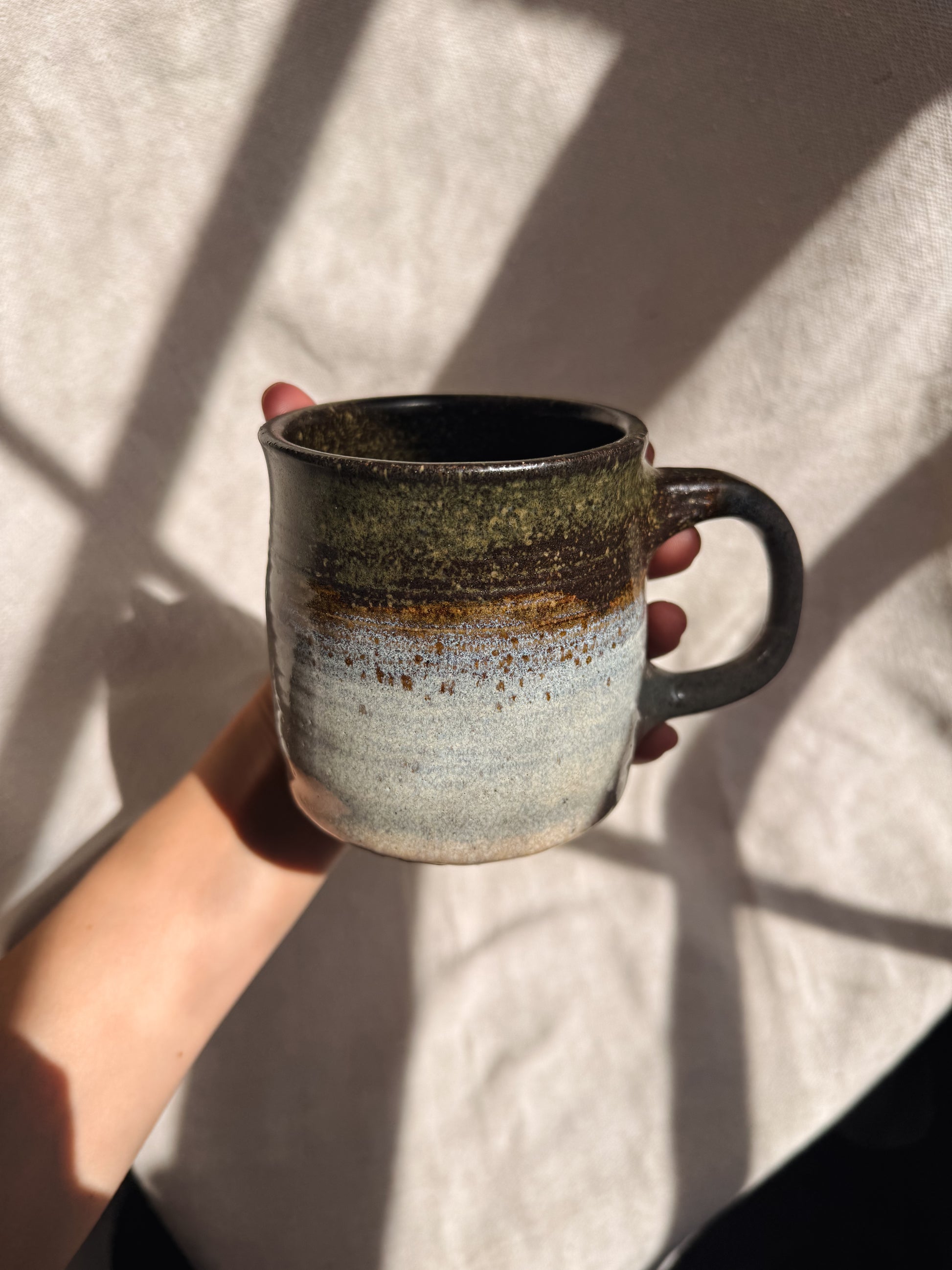 Hand holding a ceramic mug with a textured surface against a neutral background