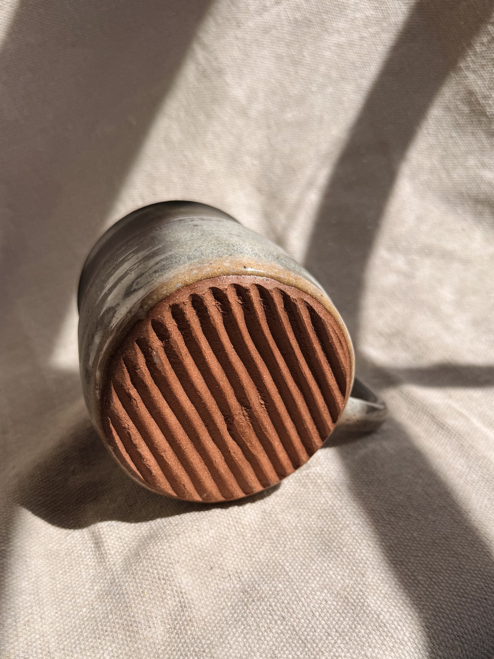 Bottom of ceramic mug with ribbed bottom texture on a textured fabric background