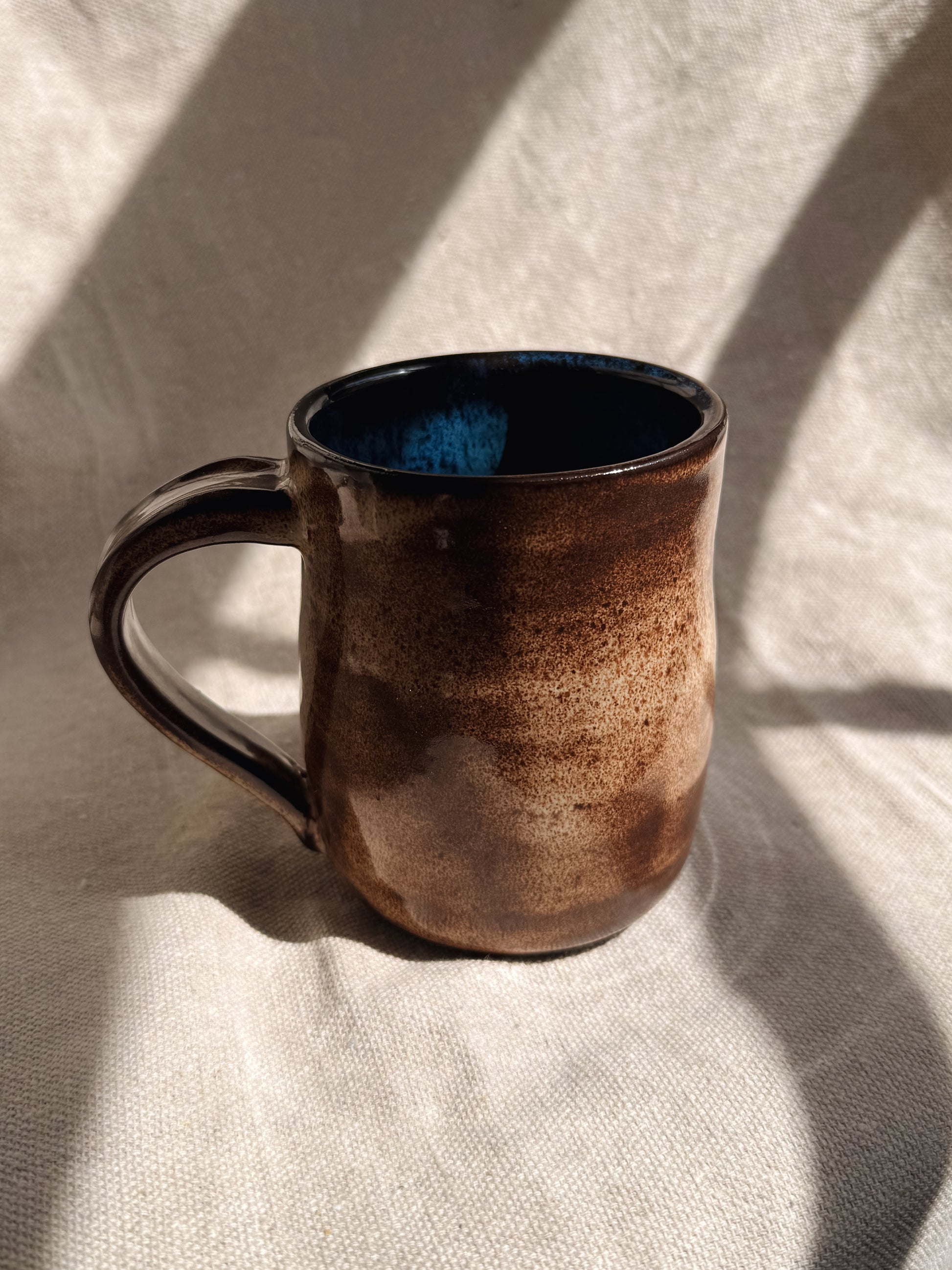 Brown ceramic mug with blue interior on a light fabric background