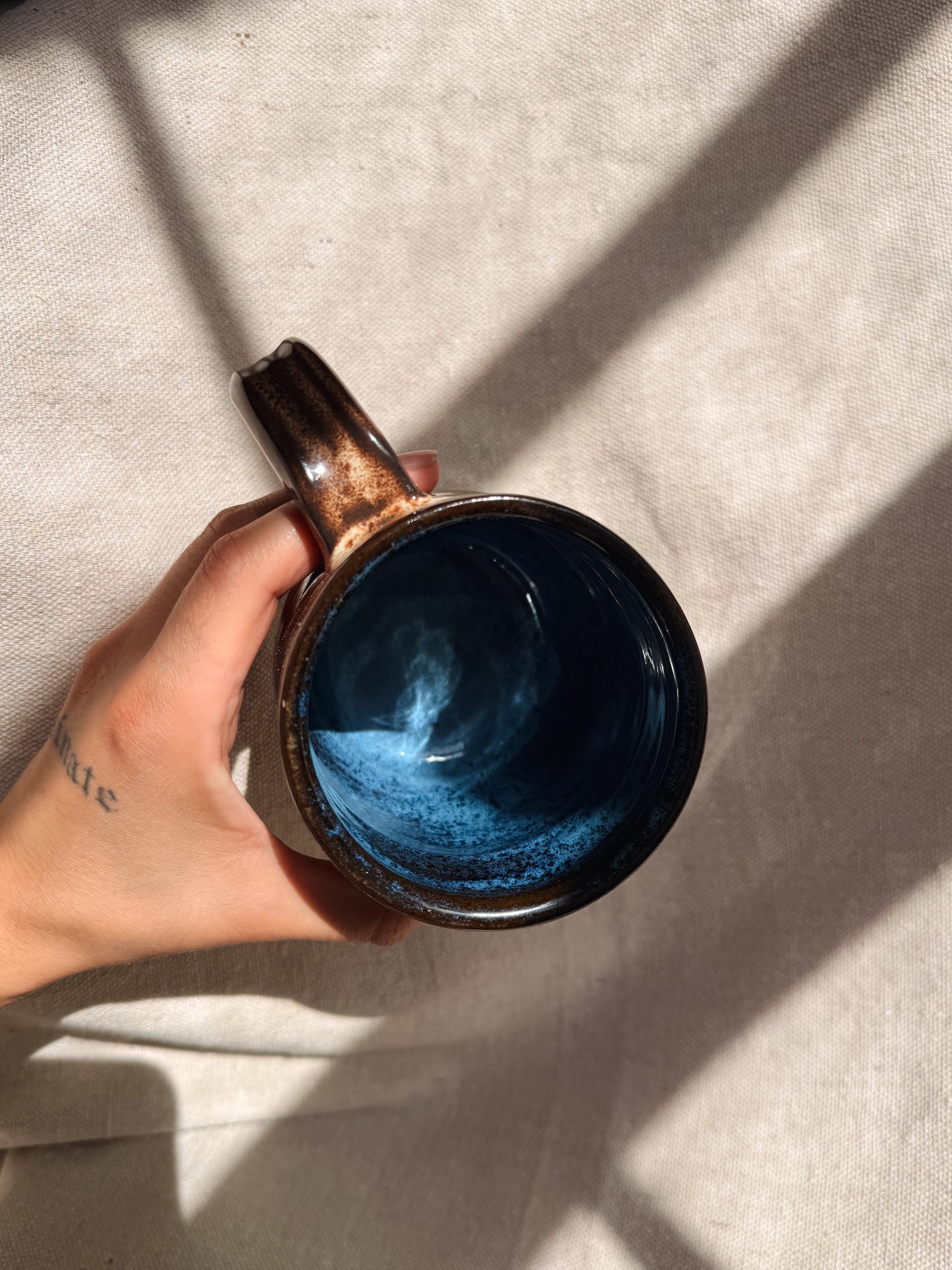 Hand holding a ceramic mug with blue interior on a light background