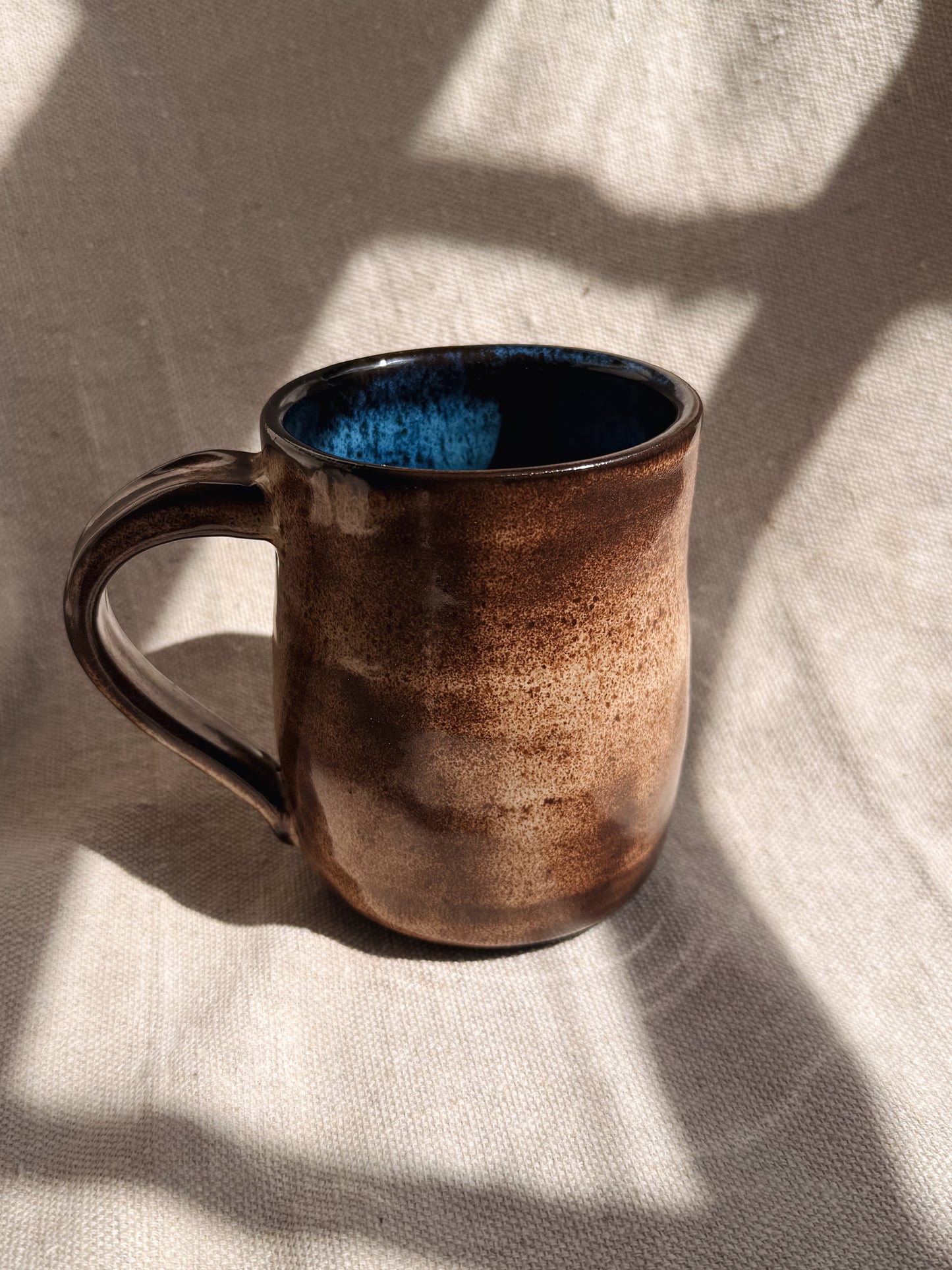 Brown ceramic mug with blue interior on a textured surface