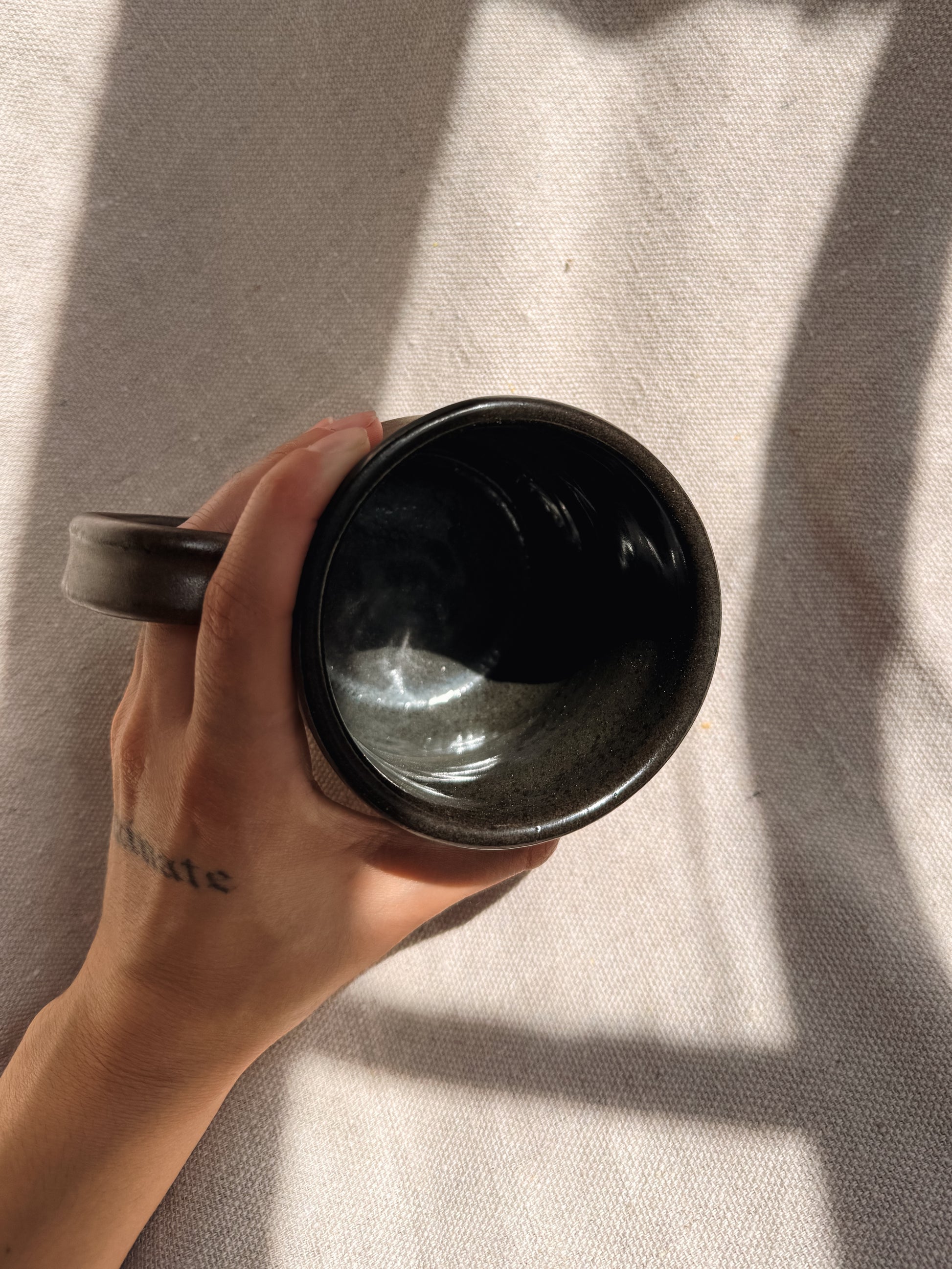Hand holding a black ceramic mug against a textured beige background